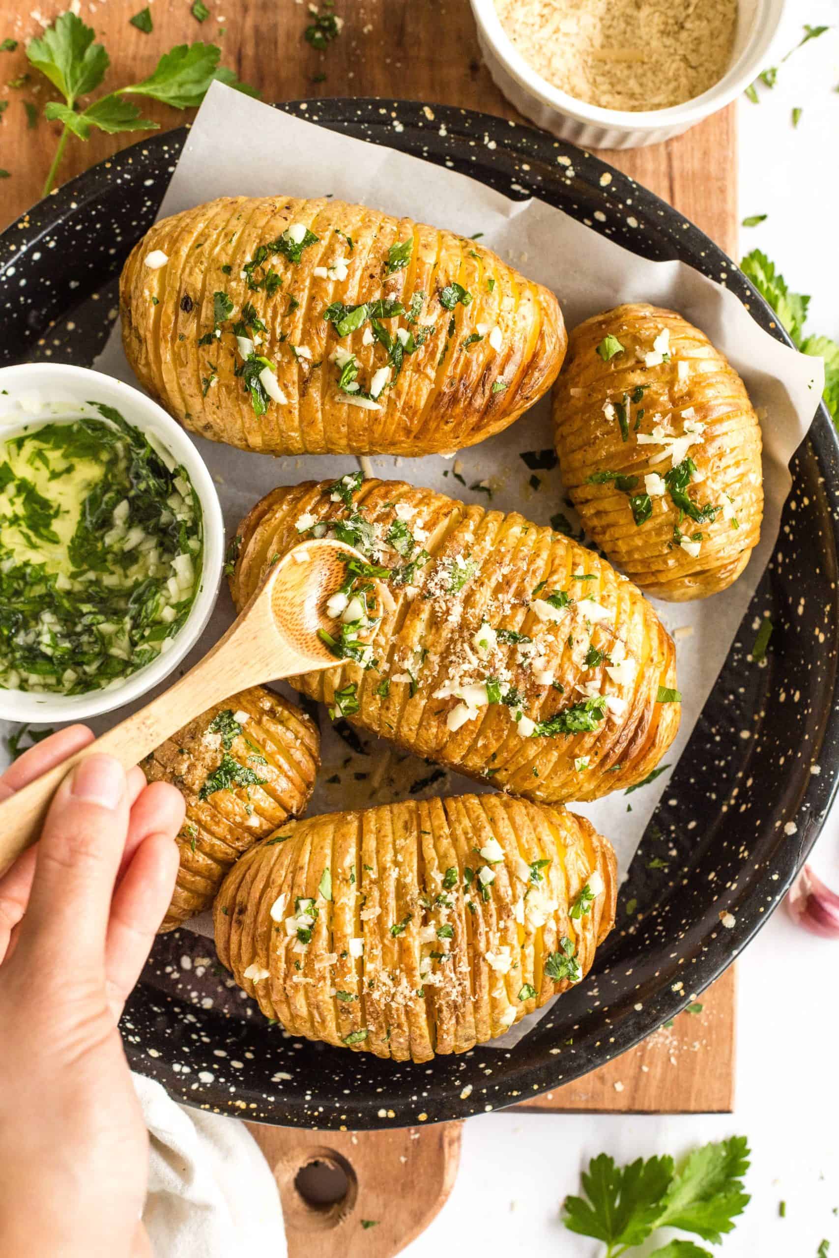 Drizzling fresh garlic and parsley on Hasselback potatoes.