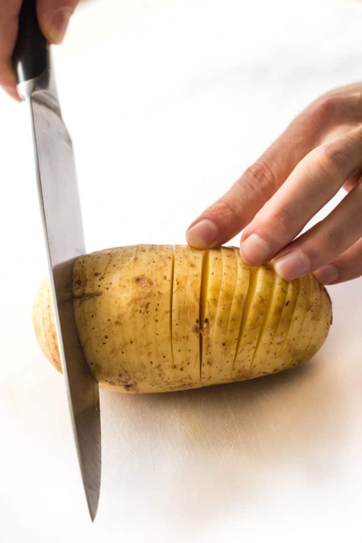 Hand slicing a yukon gold potato in thin fans to create Hasselback potatoes.