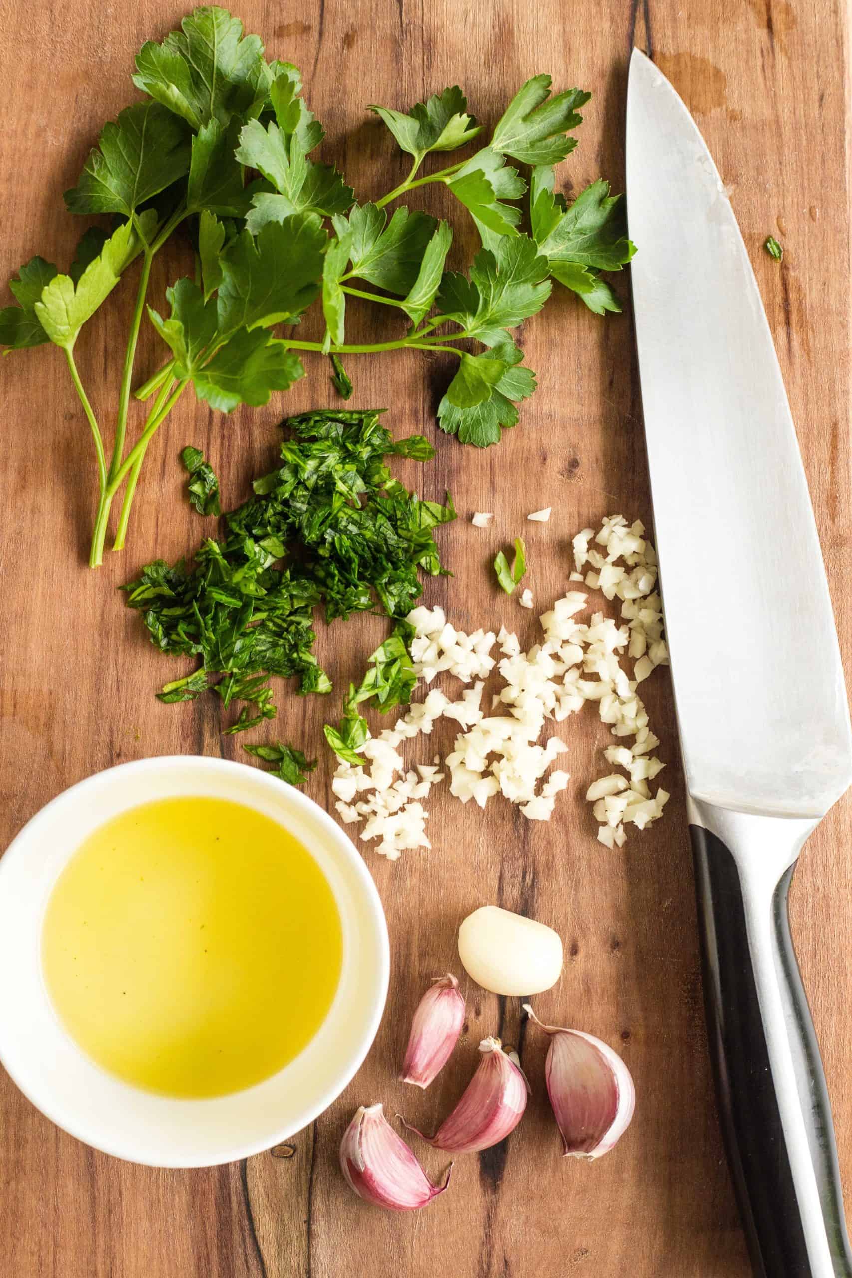 Chopped parsley, garlic and a bowl of olive oil on a wooden board.