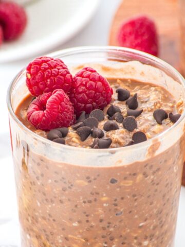 A jar of chocolate overnight oats topped with chocolate chips and raspberries