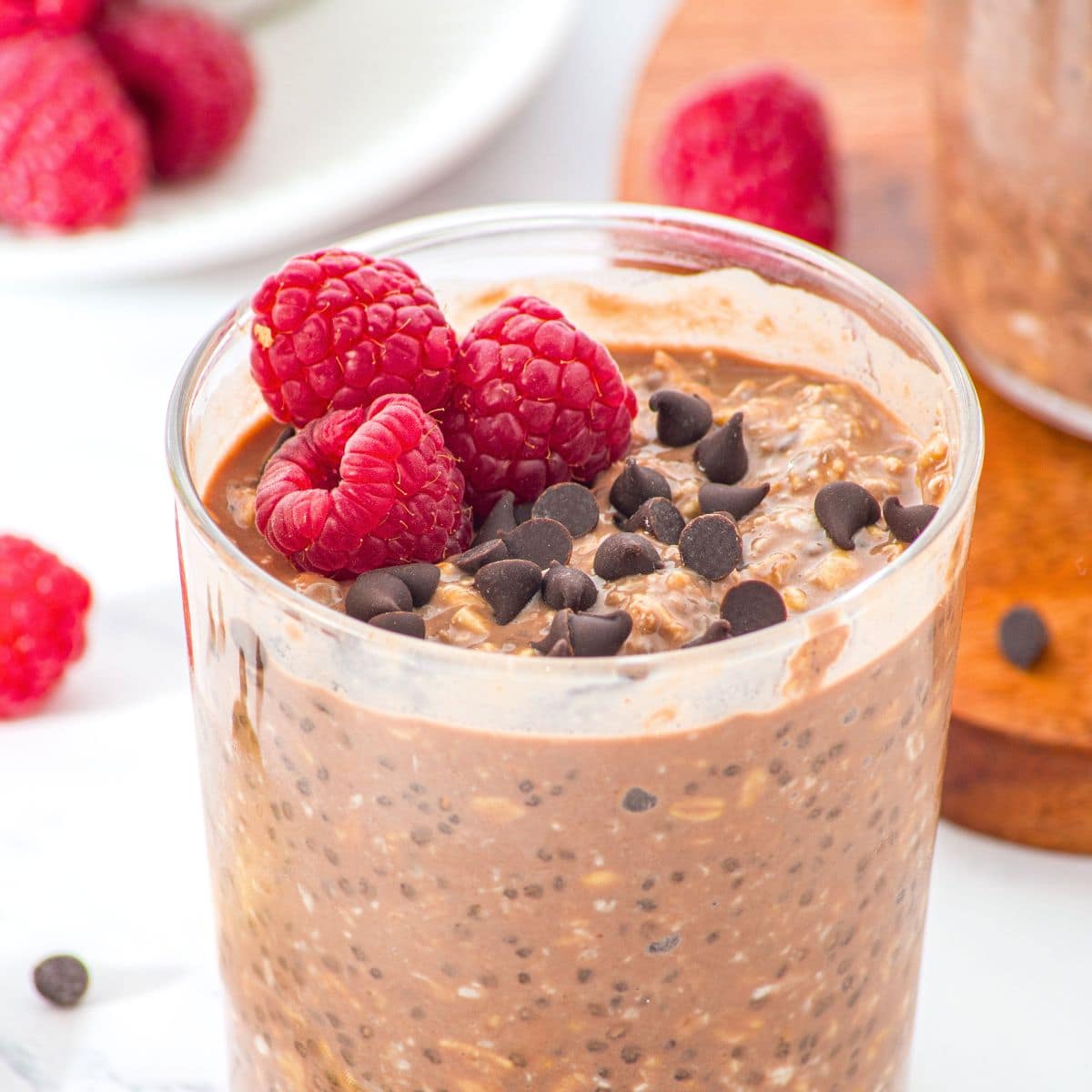 A jar of chocolate overnight oats topped with chocolate chips and raspberries