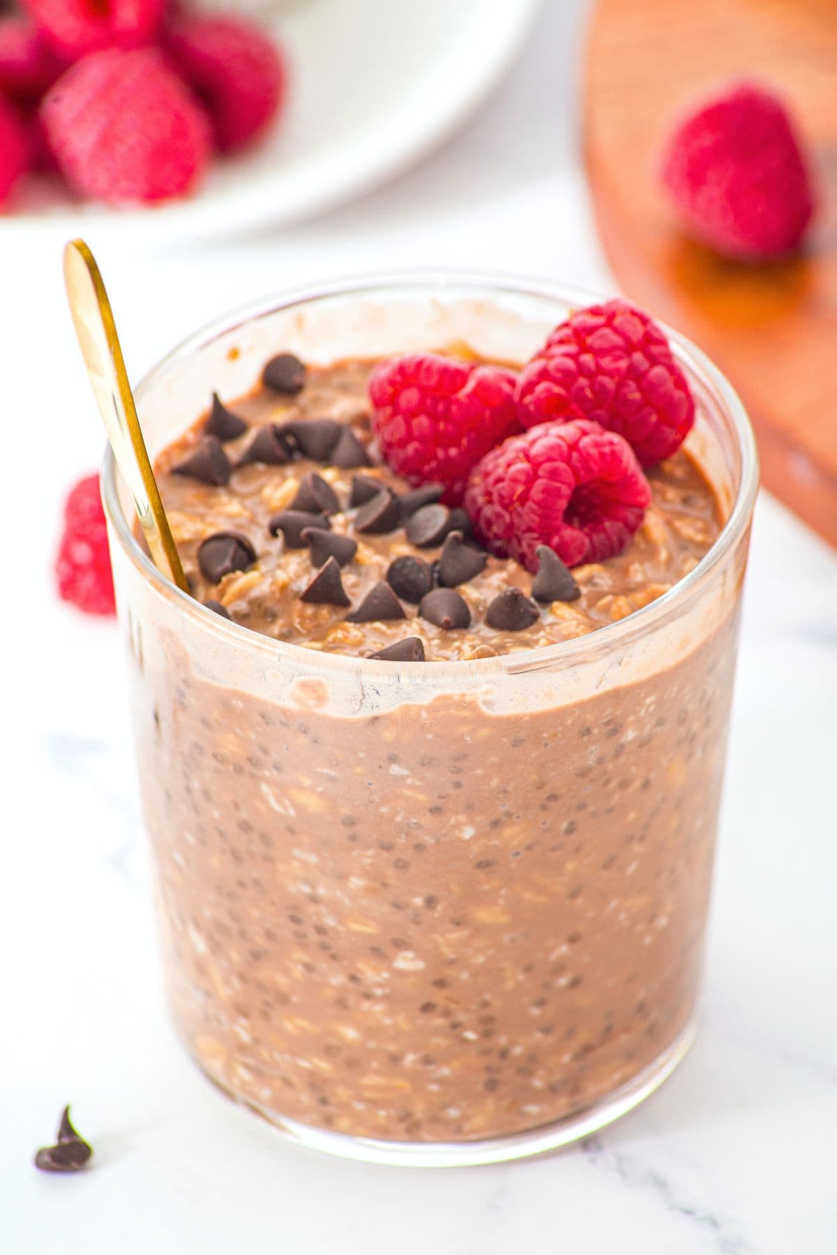 A glass of chocolate overnight oats topped with chocolate chips and raspberries.