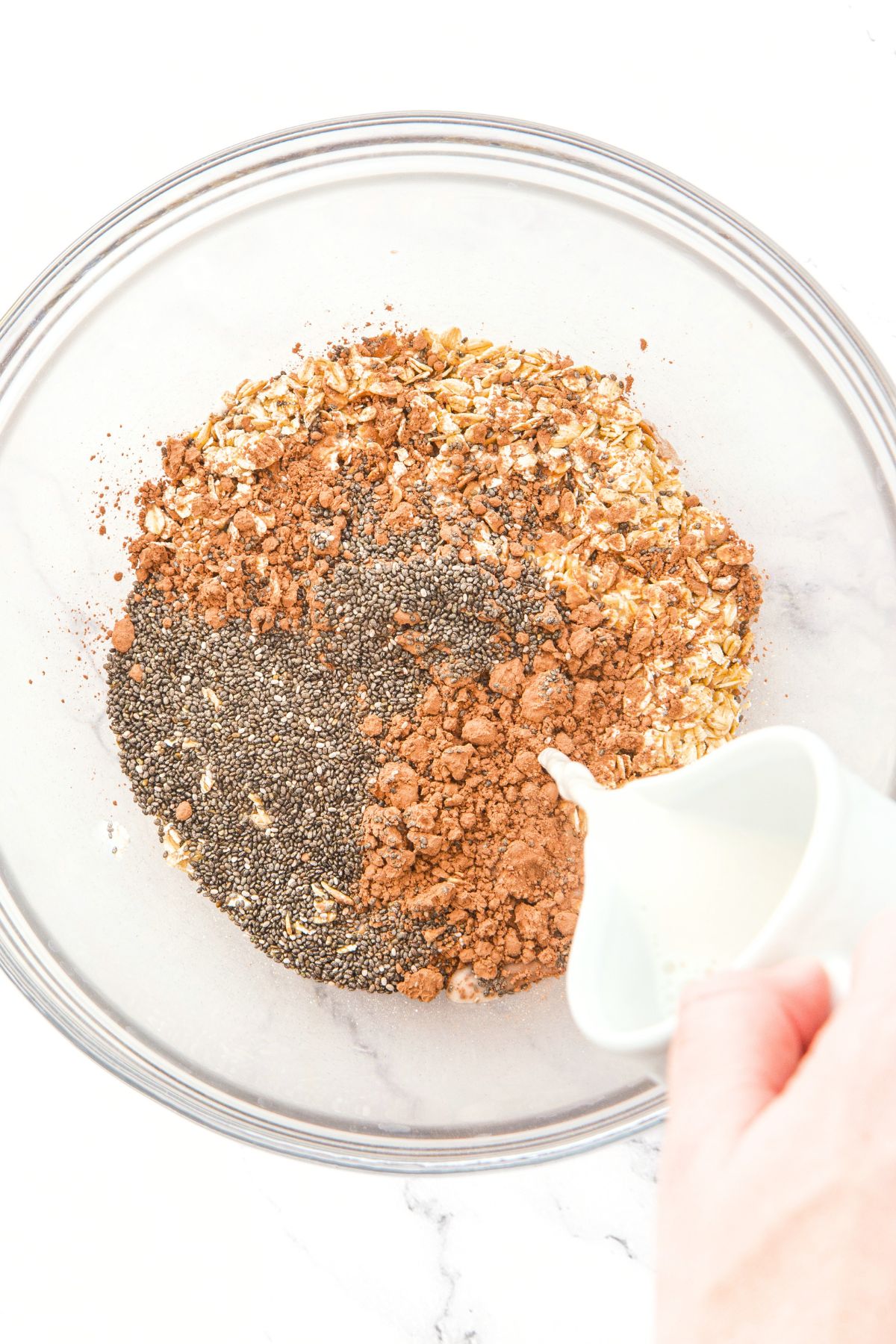 Pouring almond milk into a bowl with chia seeds, cocoa powder and rolled oats.