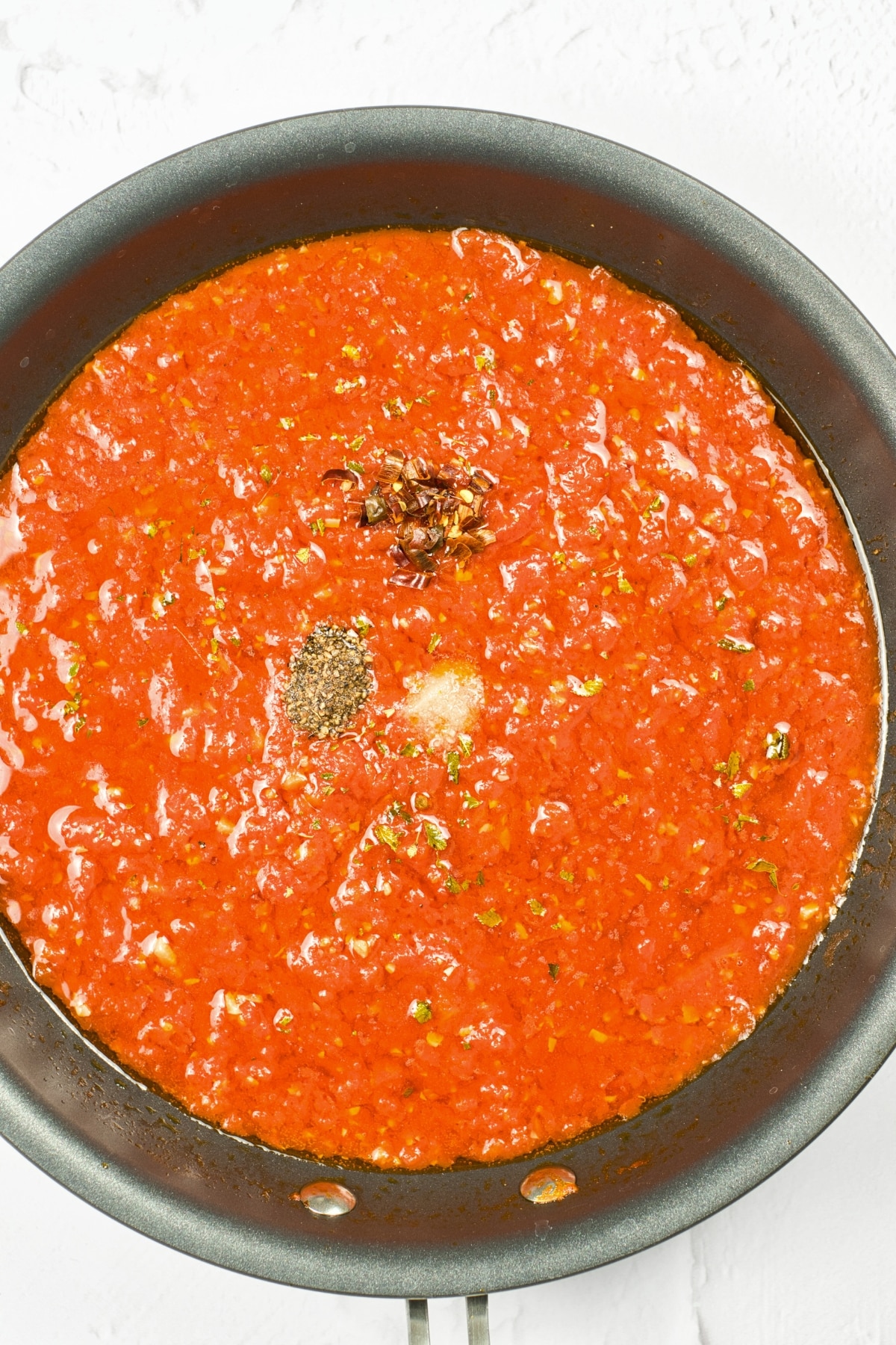 Spices and condiments on top of marinara sauce in skillet.