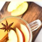 A glass of apple cider topped with cinnamon and star anise on wooden board.