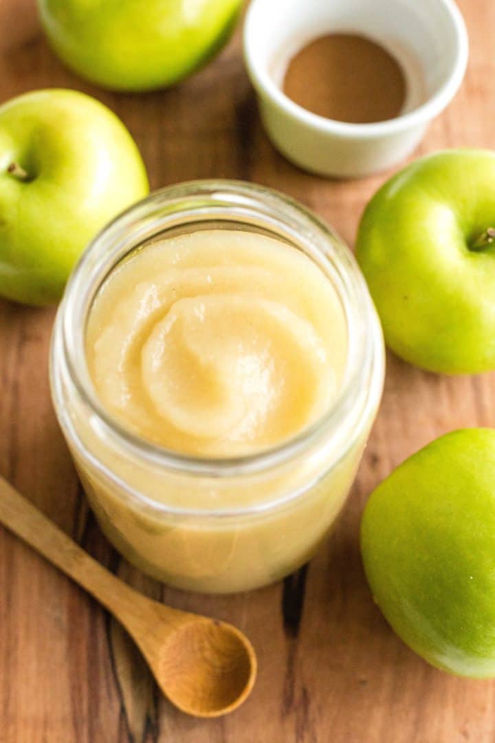 A jar of homemade applesauce surrounded by green apples