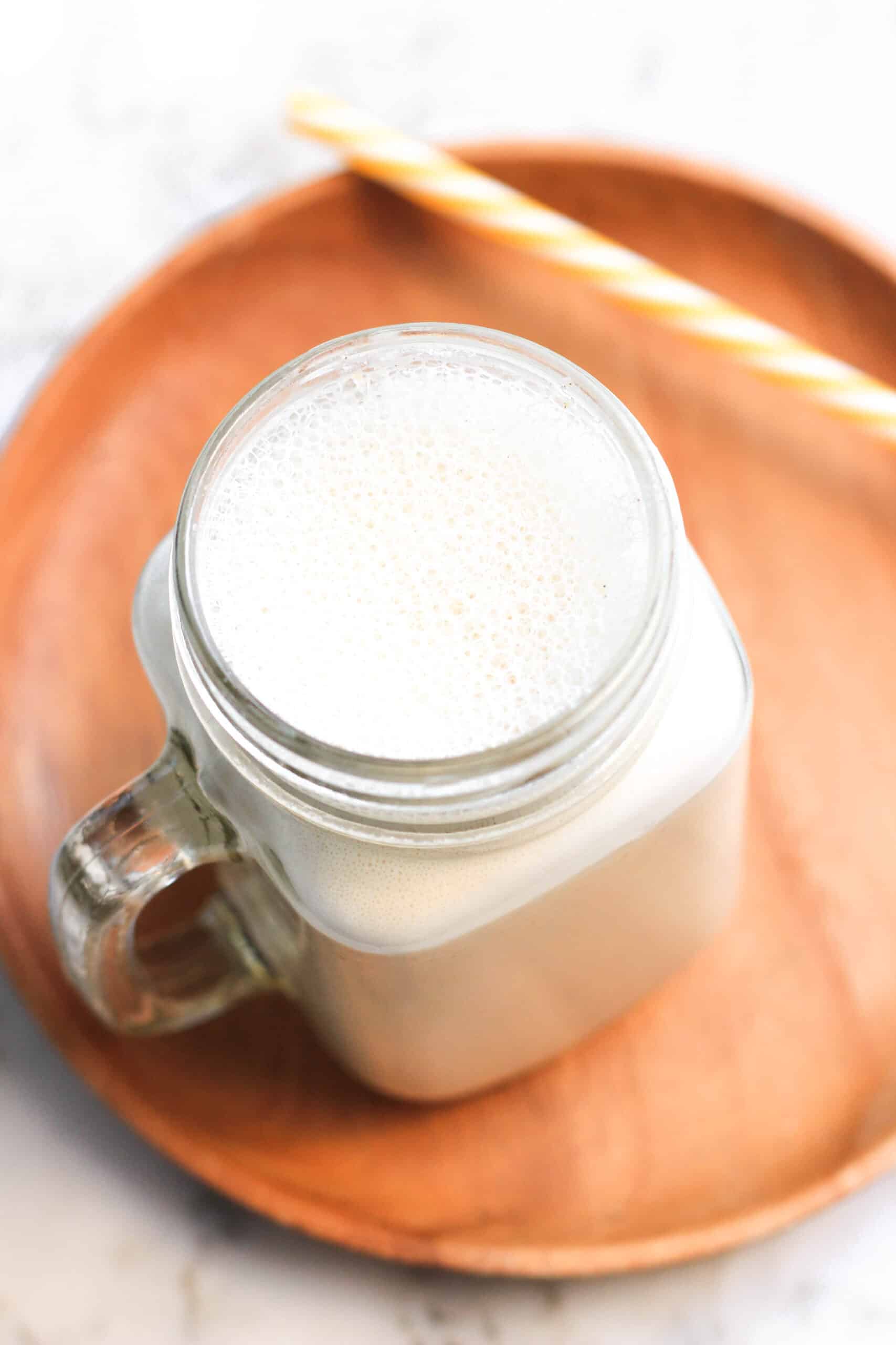 A glass mug of homemade cashew milk on a wooden plate.