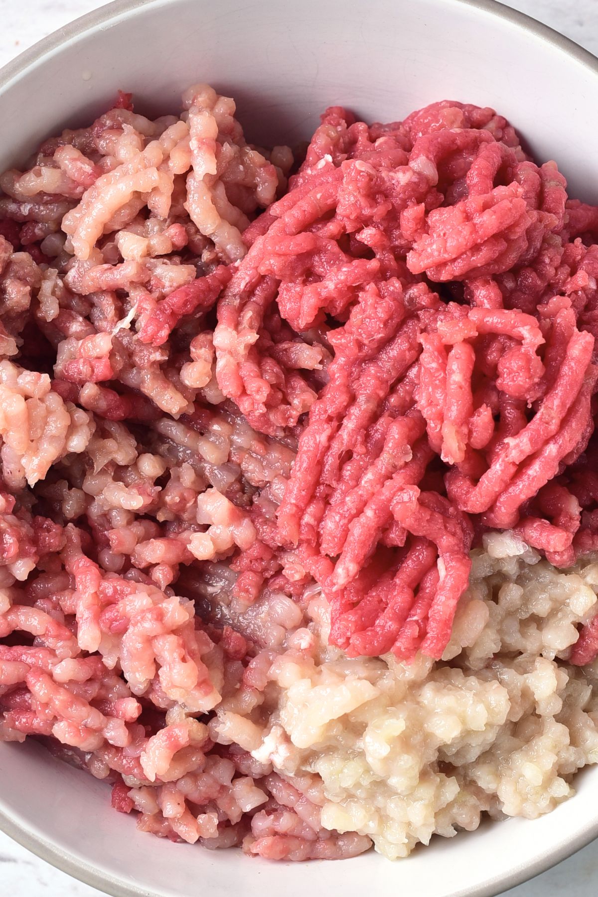 Ground beef, ground chicken and ground onion in white bowl.