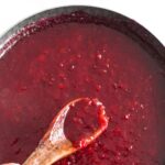 Holding up spoonful of plum jam from skillet