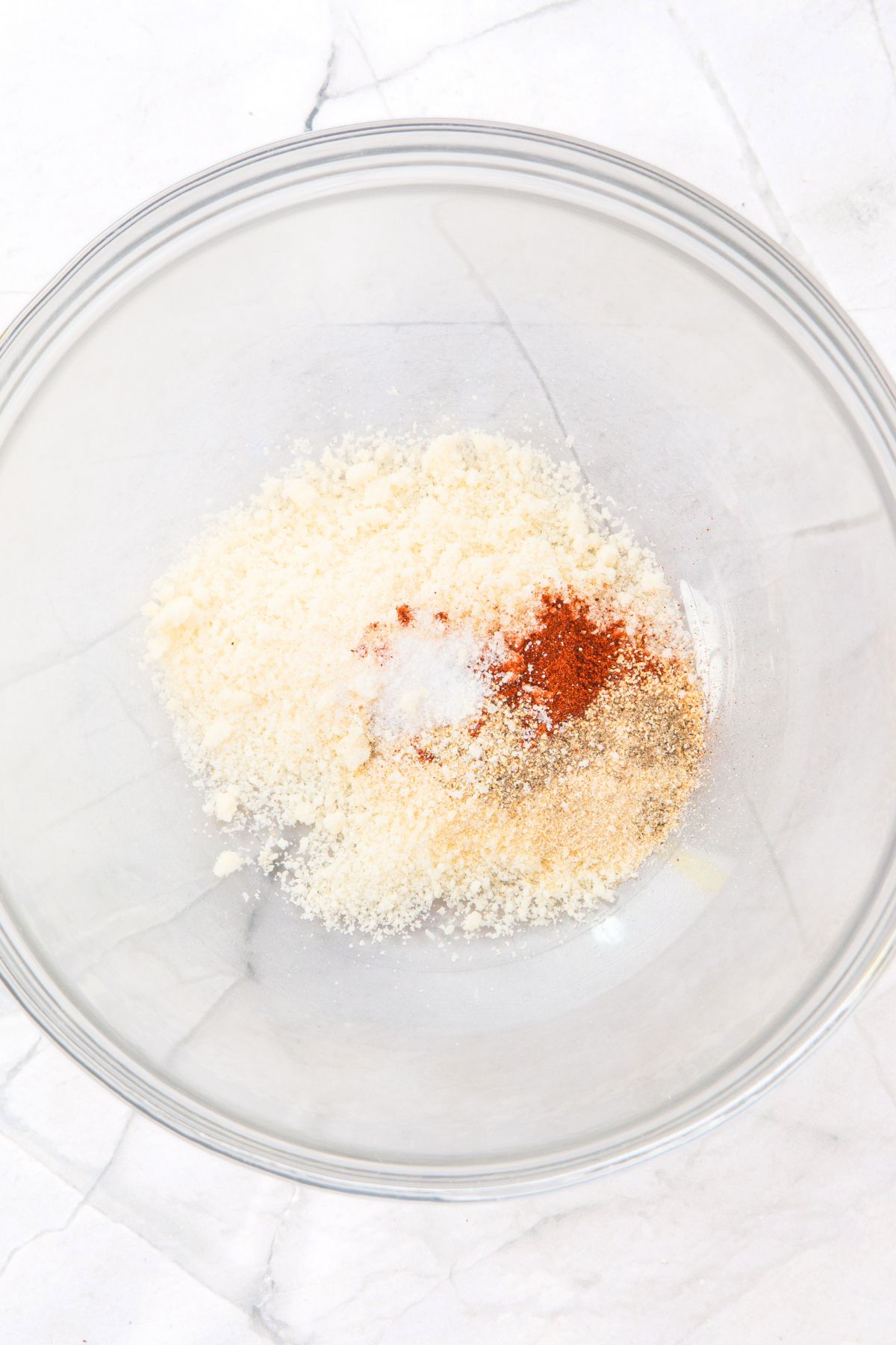 A glass bowl with grated cheese and seasonings.