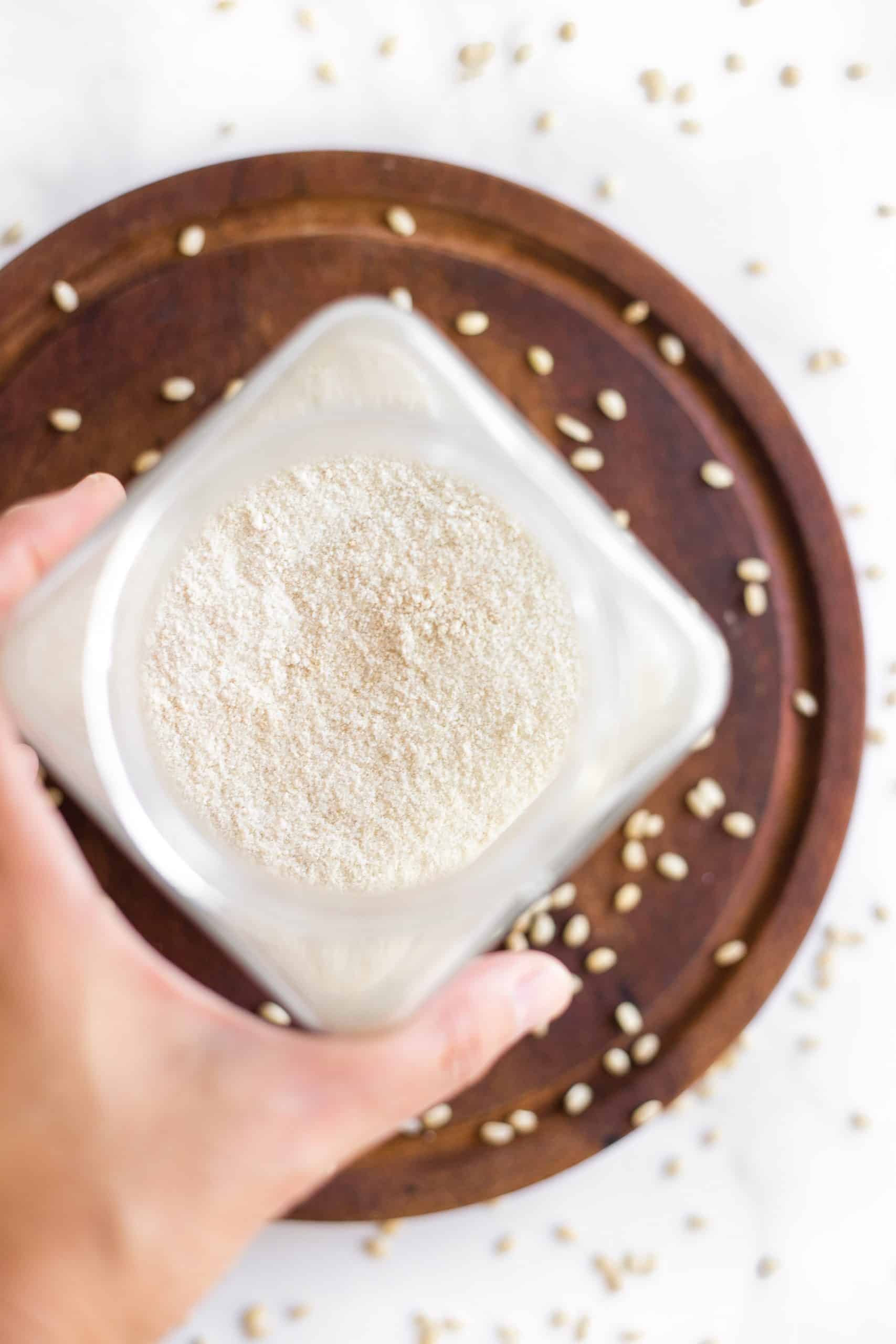 Rice flour in a jar on a round wooden board surrounded by rice grains.