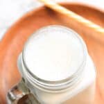 A glass mug with homemade cashew milk on wooden plate.