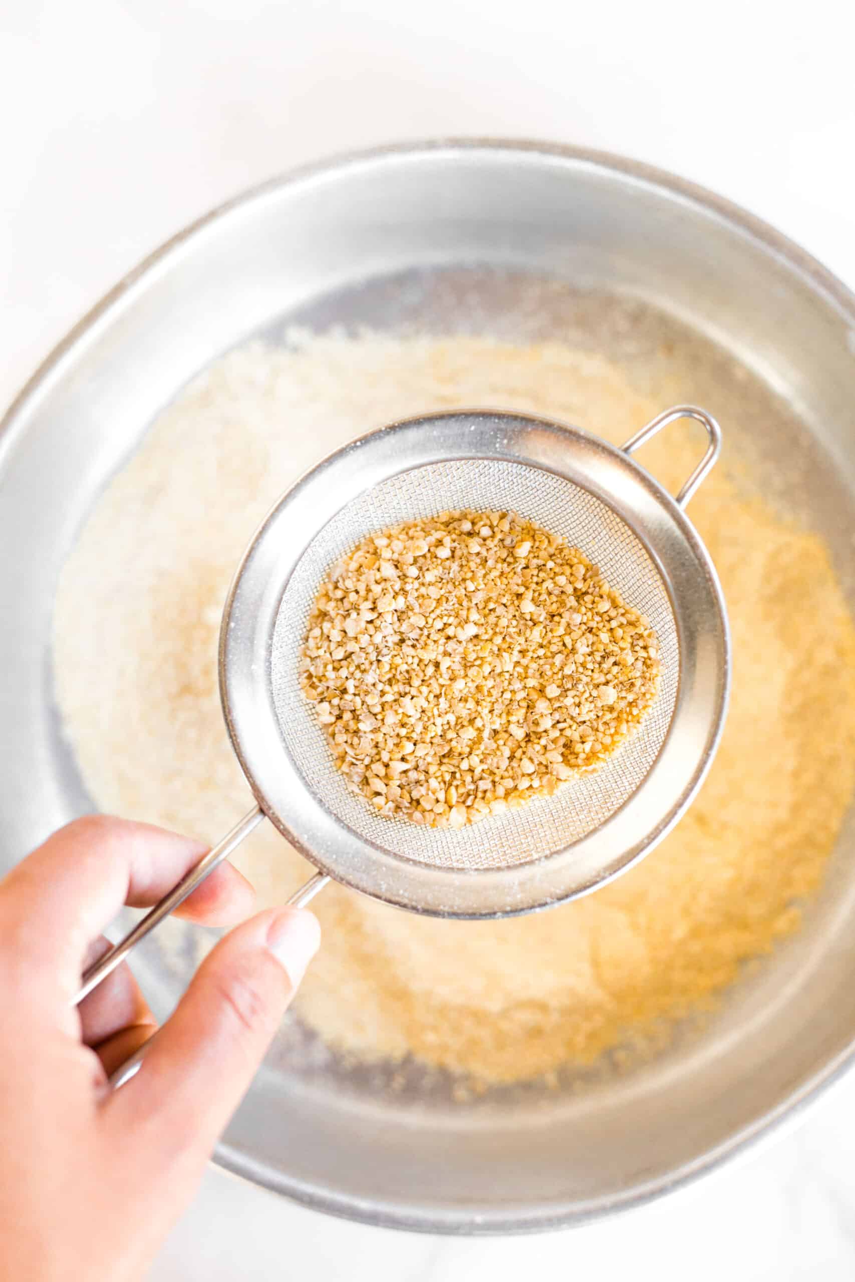 Holding up a fine mesh sieve with pieces of chickpeas.