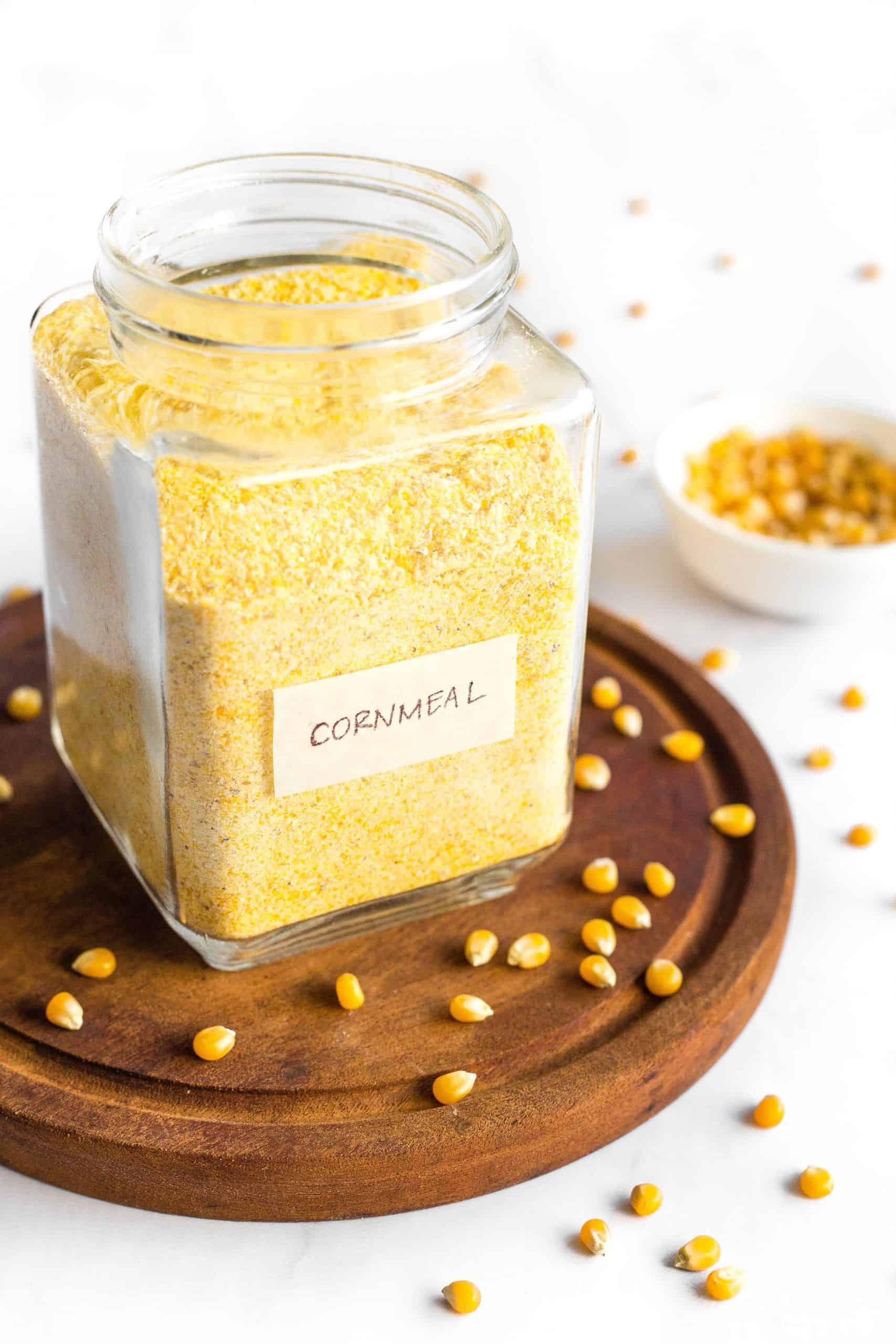 A jar of cornmeal and corn kernels on wooden board.