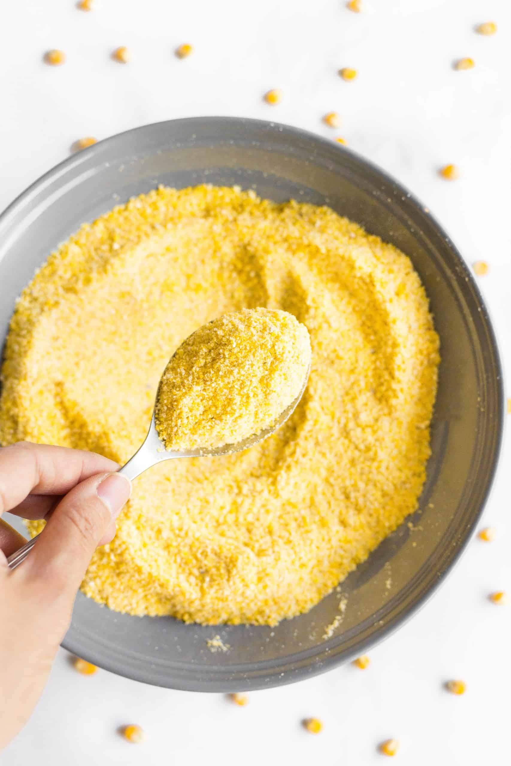 Hand holding up a spoonful of homemade cornmeal from a bowl.