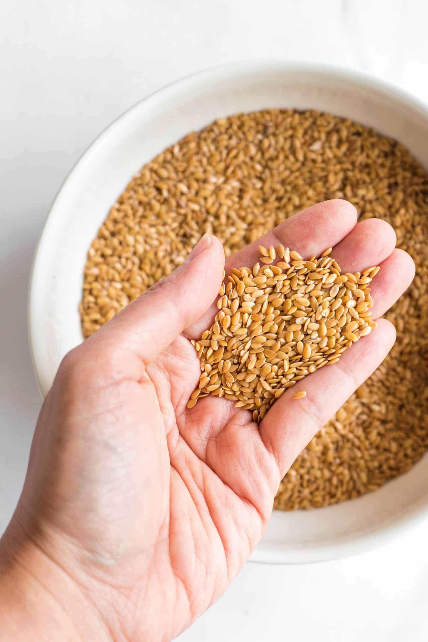 Hand holding up a handful of golden flax seeds from a bowl.