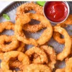 Top down view of gluten-free onion rings on parchment-lined plate.