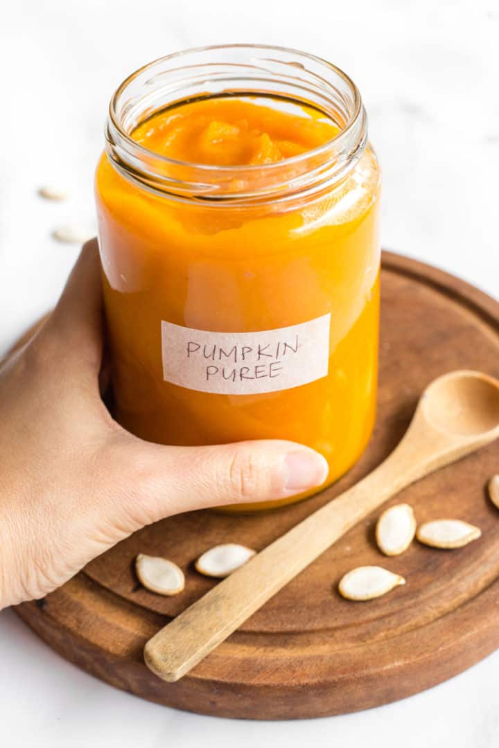 Hand holding a jar of homemade pumpkin puree.