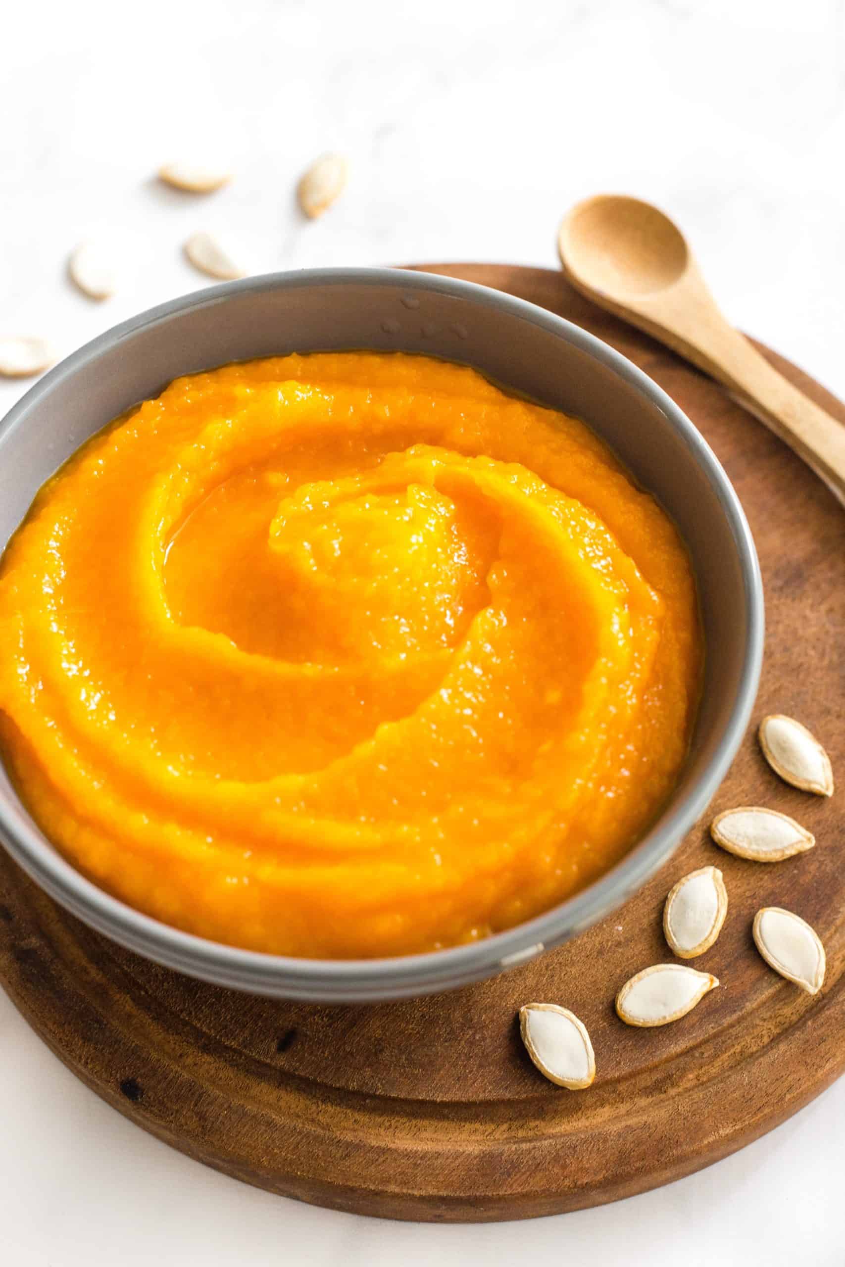 Pumpkin puree in a grey bowl on a round wooden board.