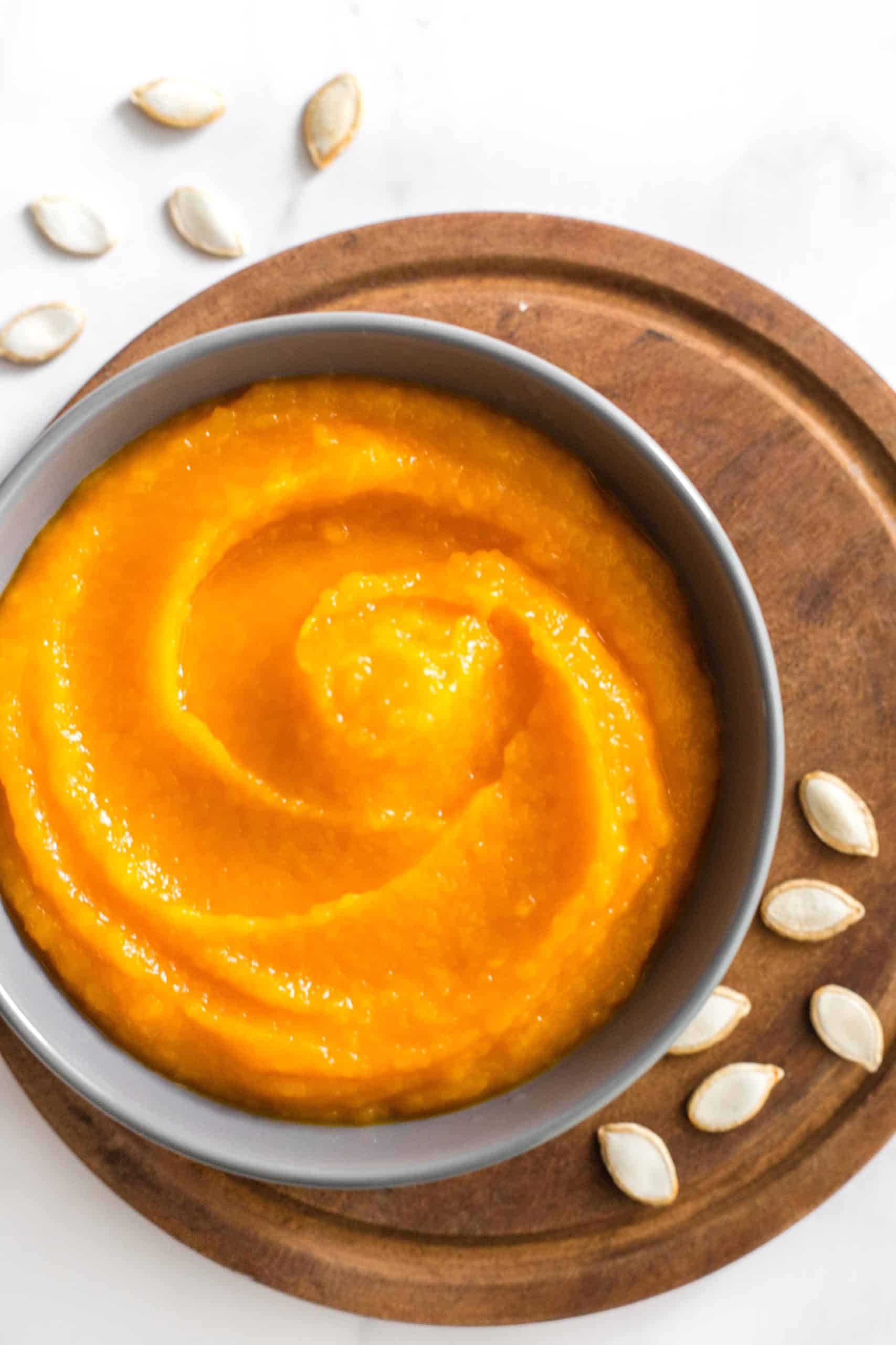 A grey bowl of homemade pumpkin puree on a wooden board.