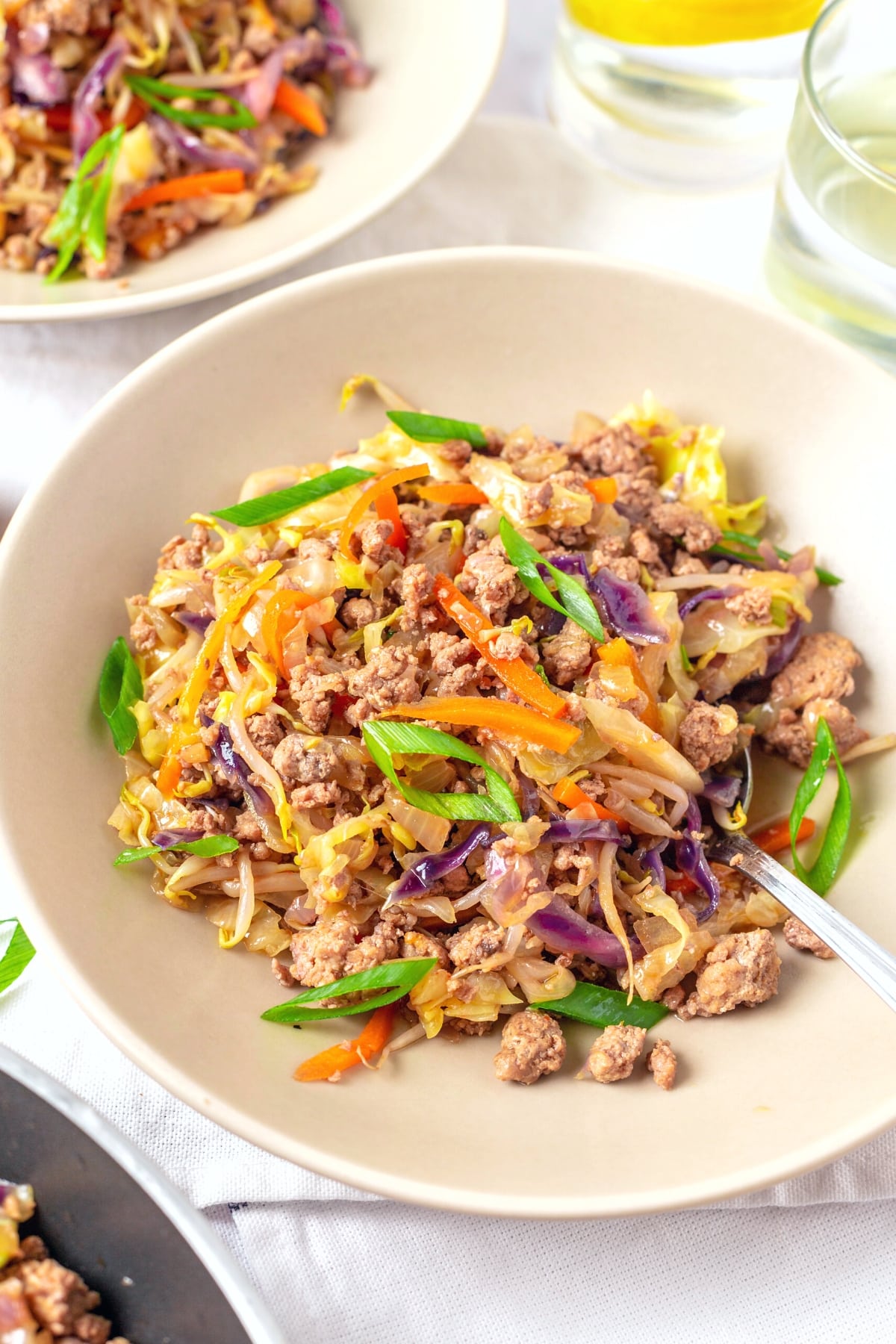 A bowl of sautéed minced meat with veggies with a spoon.