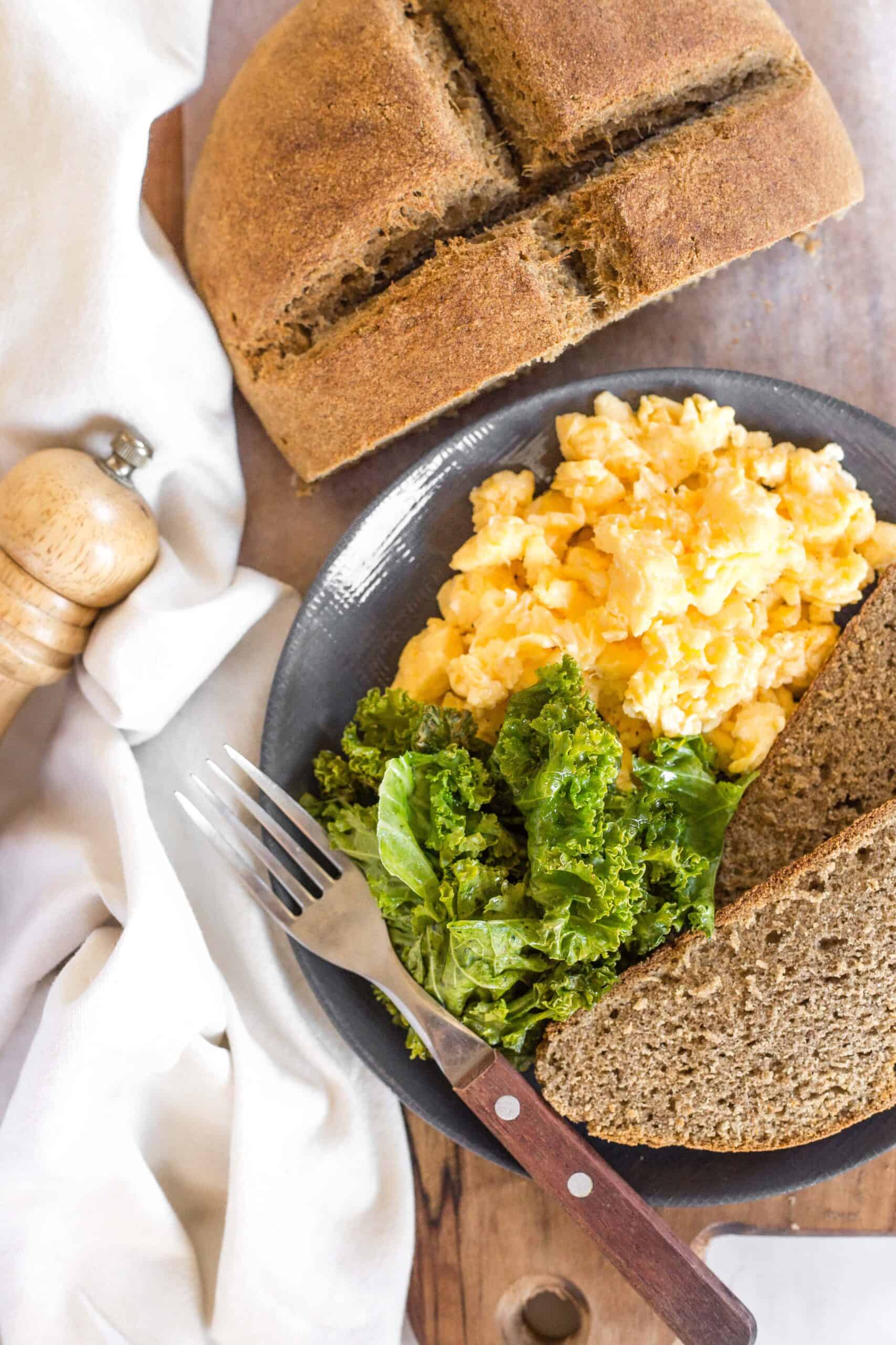 A plate of sautéed kale, scrambled eggs and two slices of Irish brown bread.