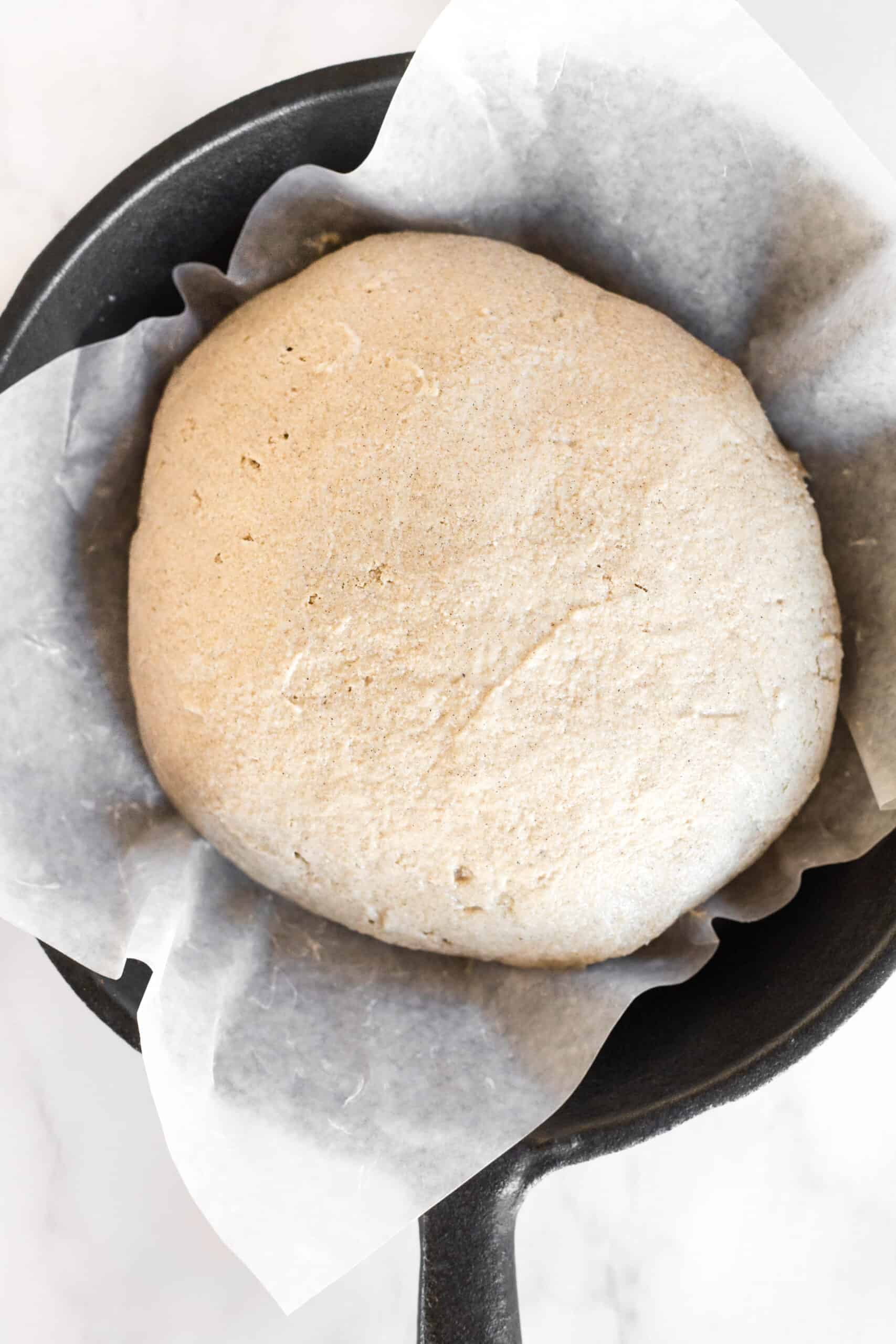Brown bread dough in parchment-lined cast iron pan