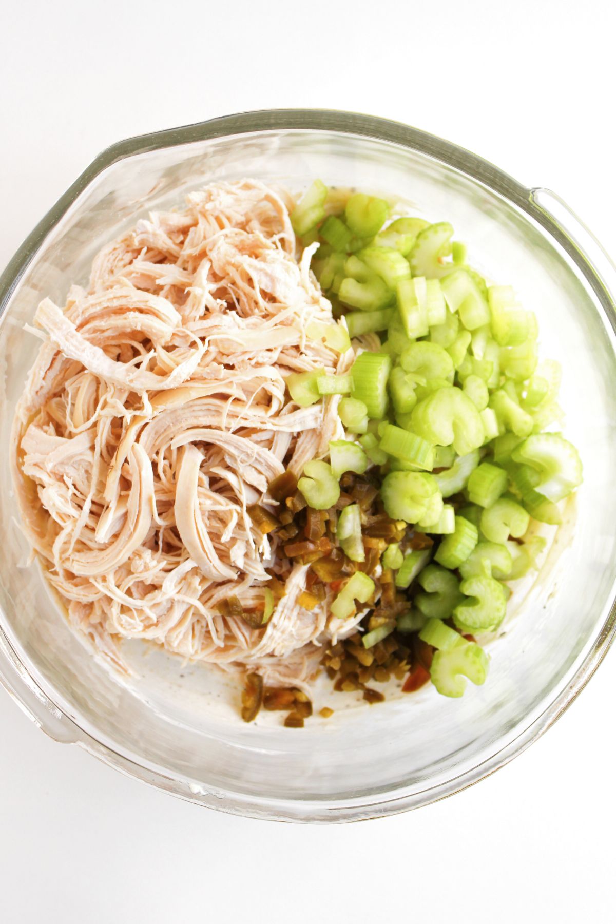 A bowl with diced celery, shredded chicken, and pickled jalapeños.