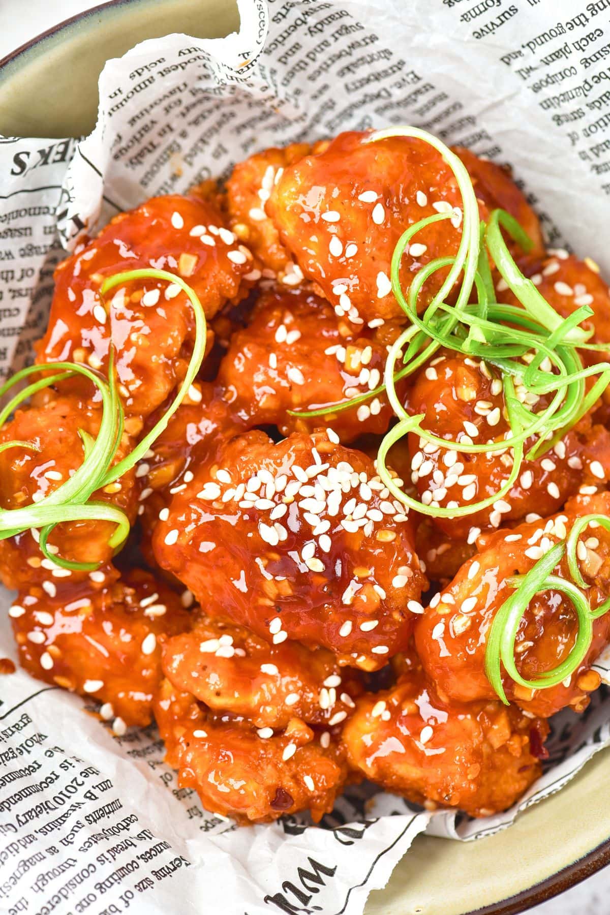 A bowl of Korean fried chicken topped with sesame seeds and green onions