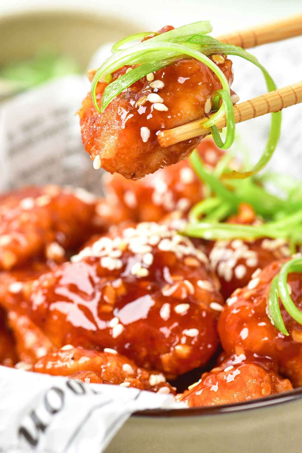 Chopsticks holding up a piece of sesame sprinkled fried chicken in sauce