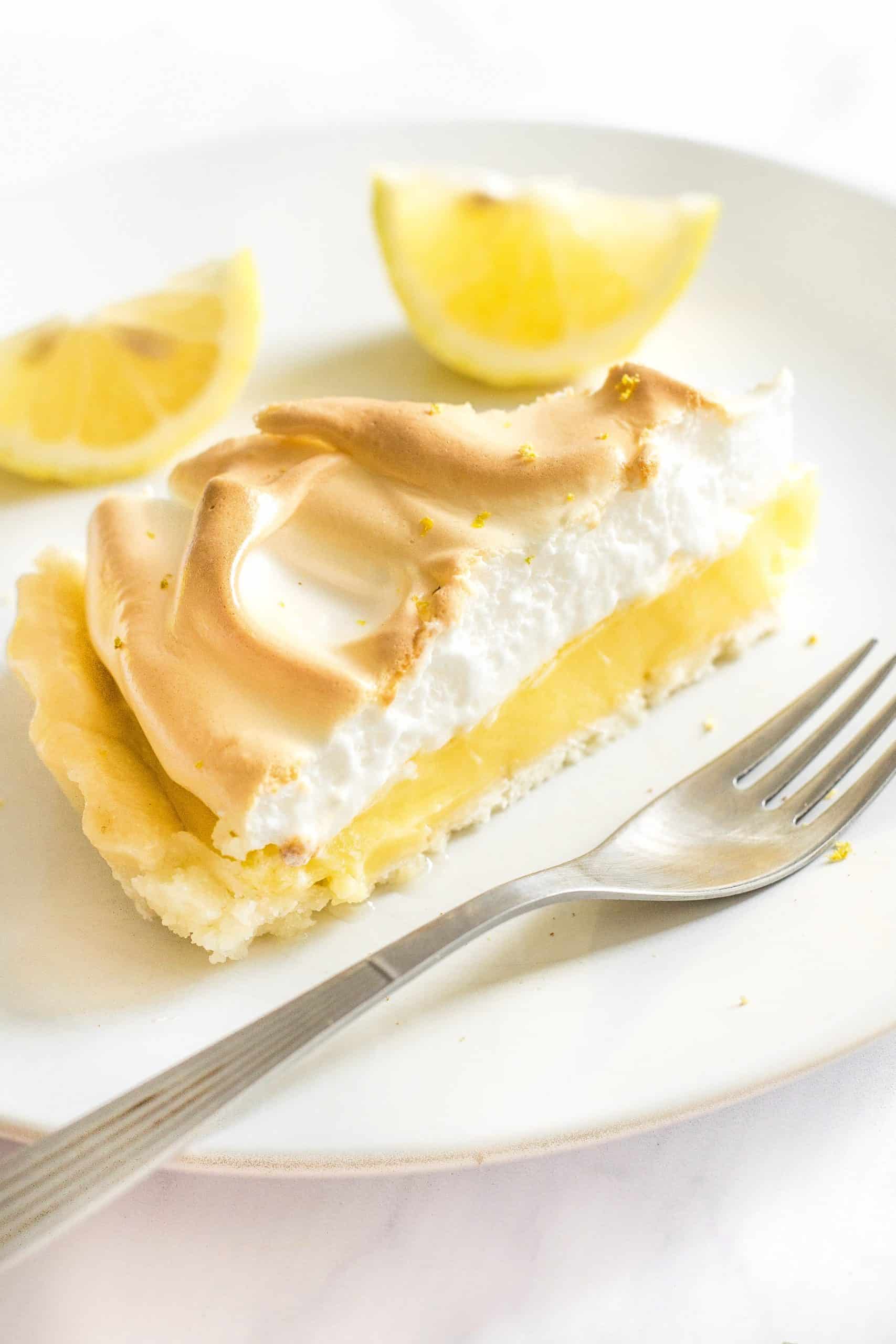 A close up of a slice of gluten-free lemon meringue pie and a fork on a plate.
