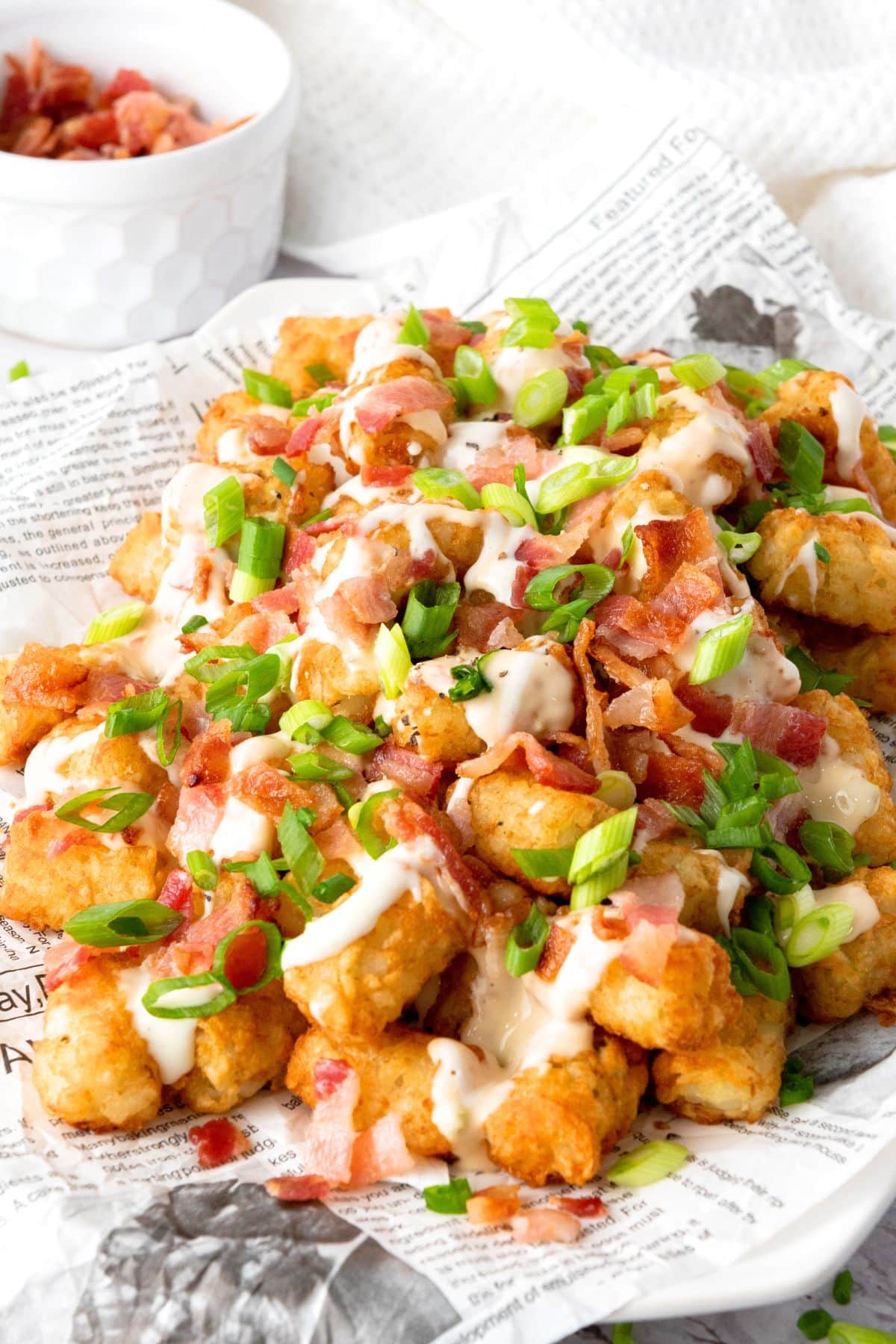 Loaded tater tots on parchment paper with bowl of bacon.