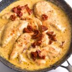A skillet with chicken and sun dried tomatoes in creamy sauce