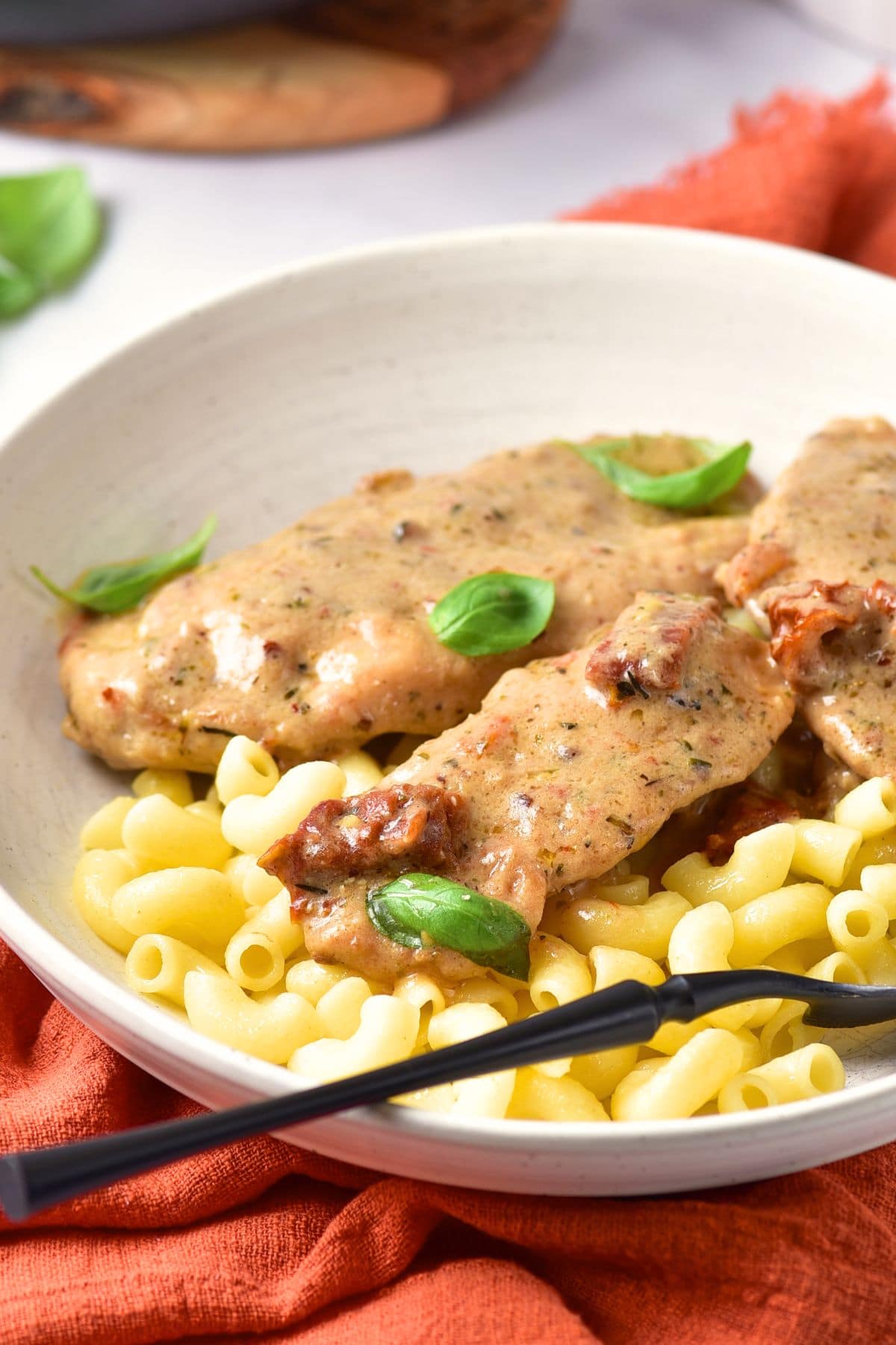 A bowl of pasta topped with with chicken breasts and sundried tomatoes
