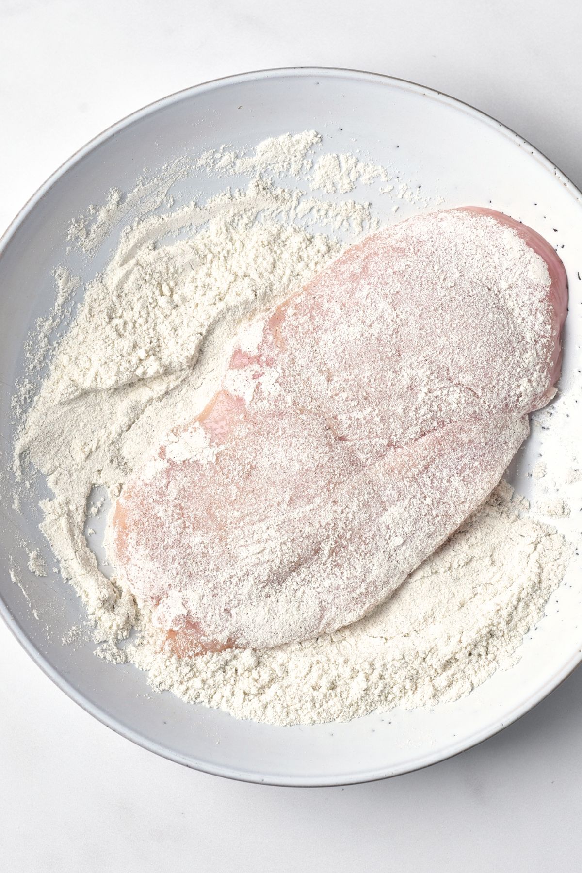 Coating chicken breast with flour mixture in bowl.