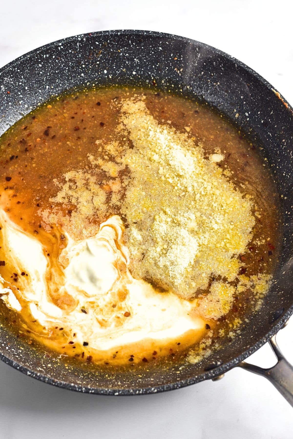 Heavy cream and grated parmesan cheese in a skillet with chicken broth