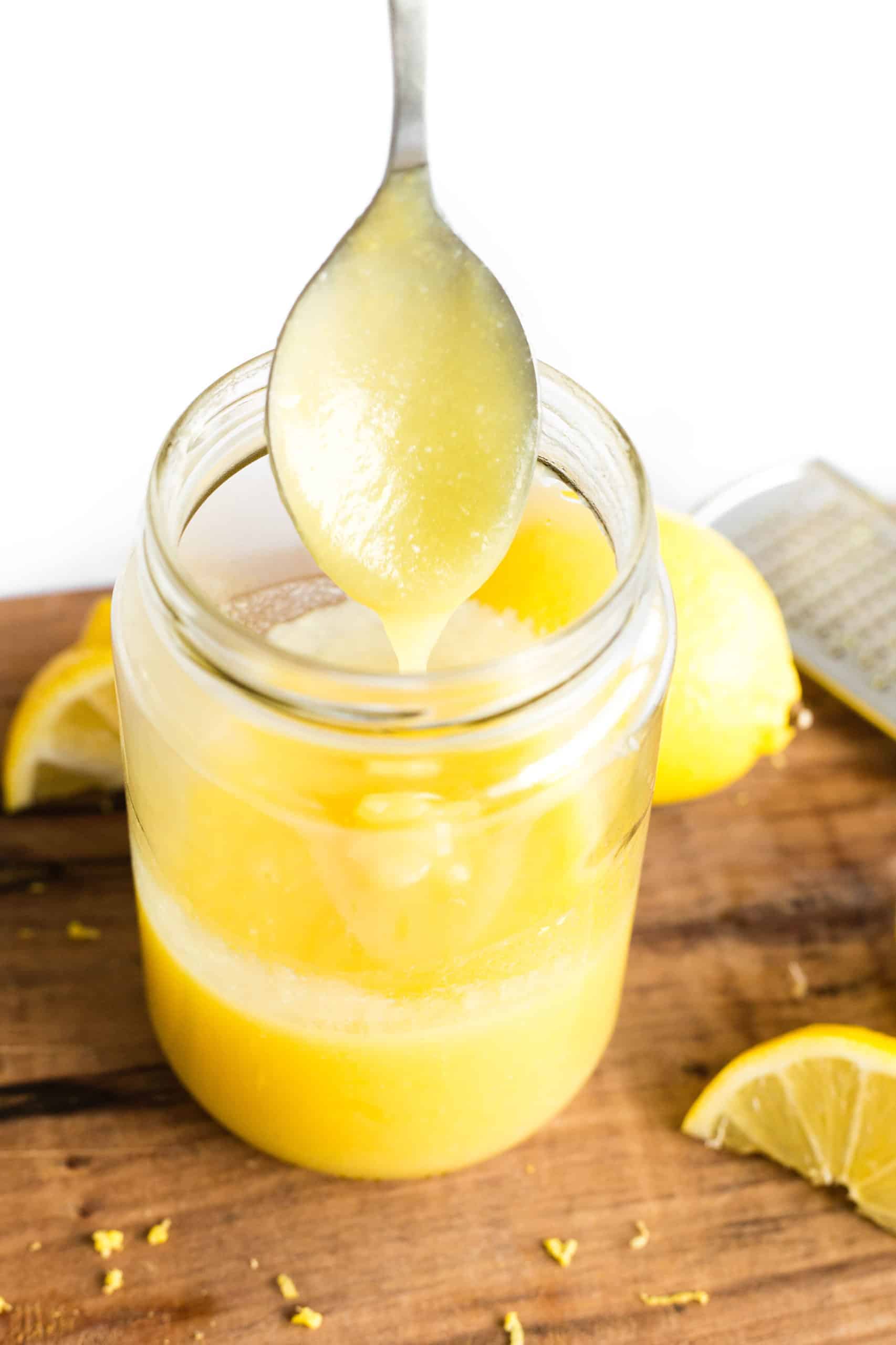 Hand holding up a spoon of microwave lemon curd dripping into a glass jar.