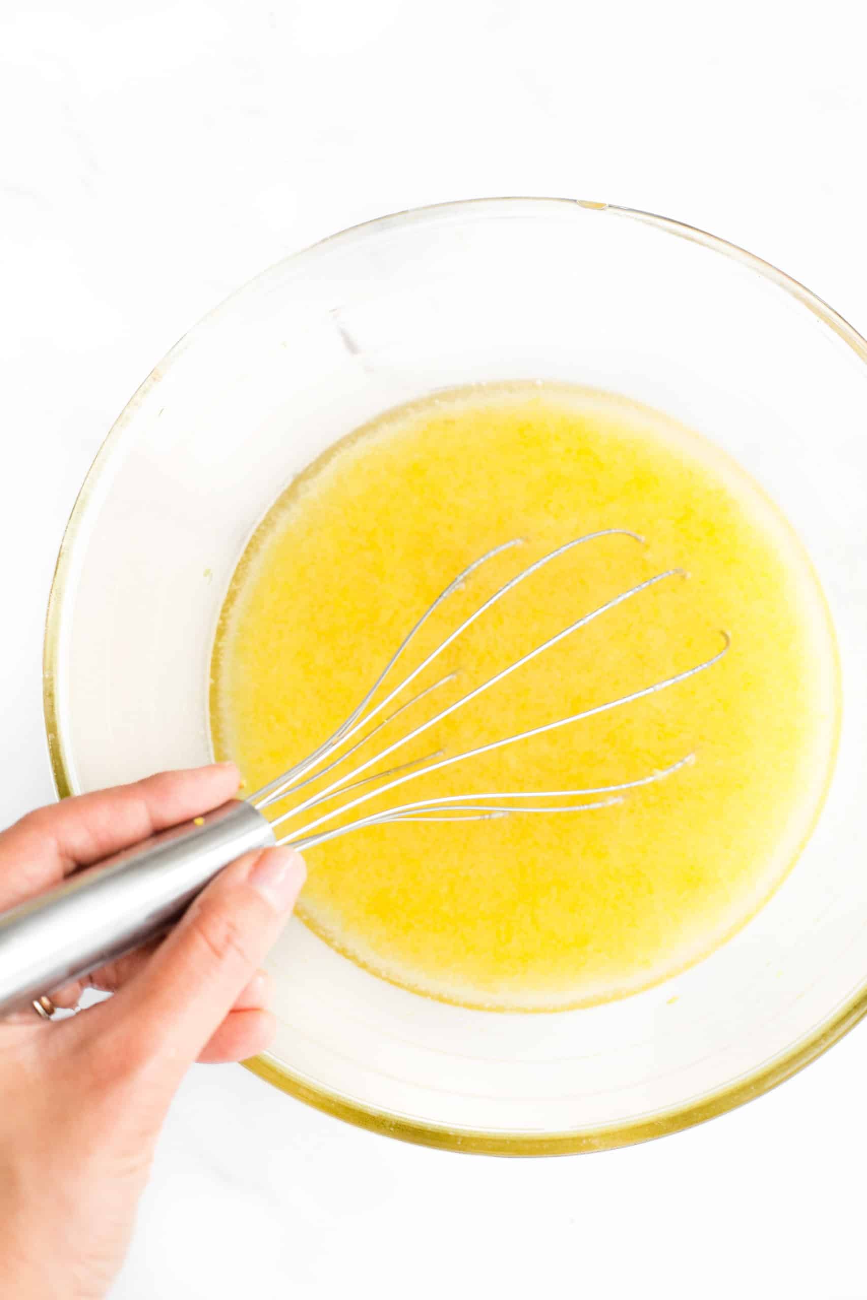 Hand whisking lemon curd ingredients in a large glass bowl.