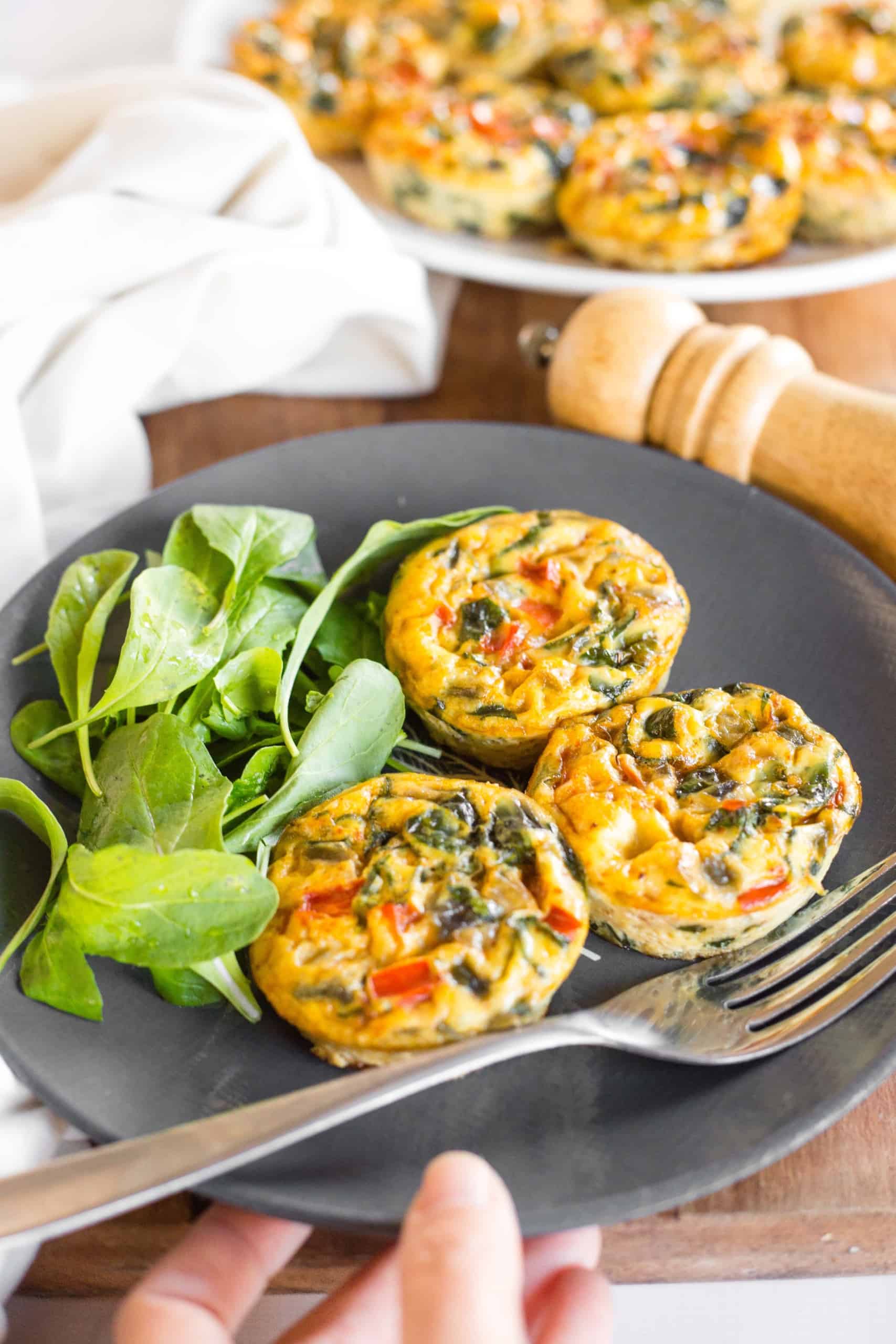 Hand reaching for a plate of crustless mini vegetable quiches and salad on the side.