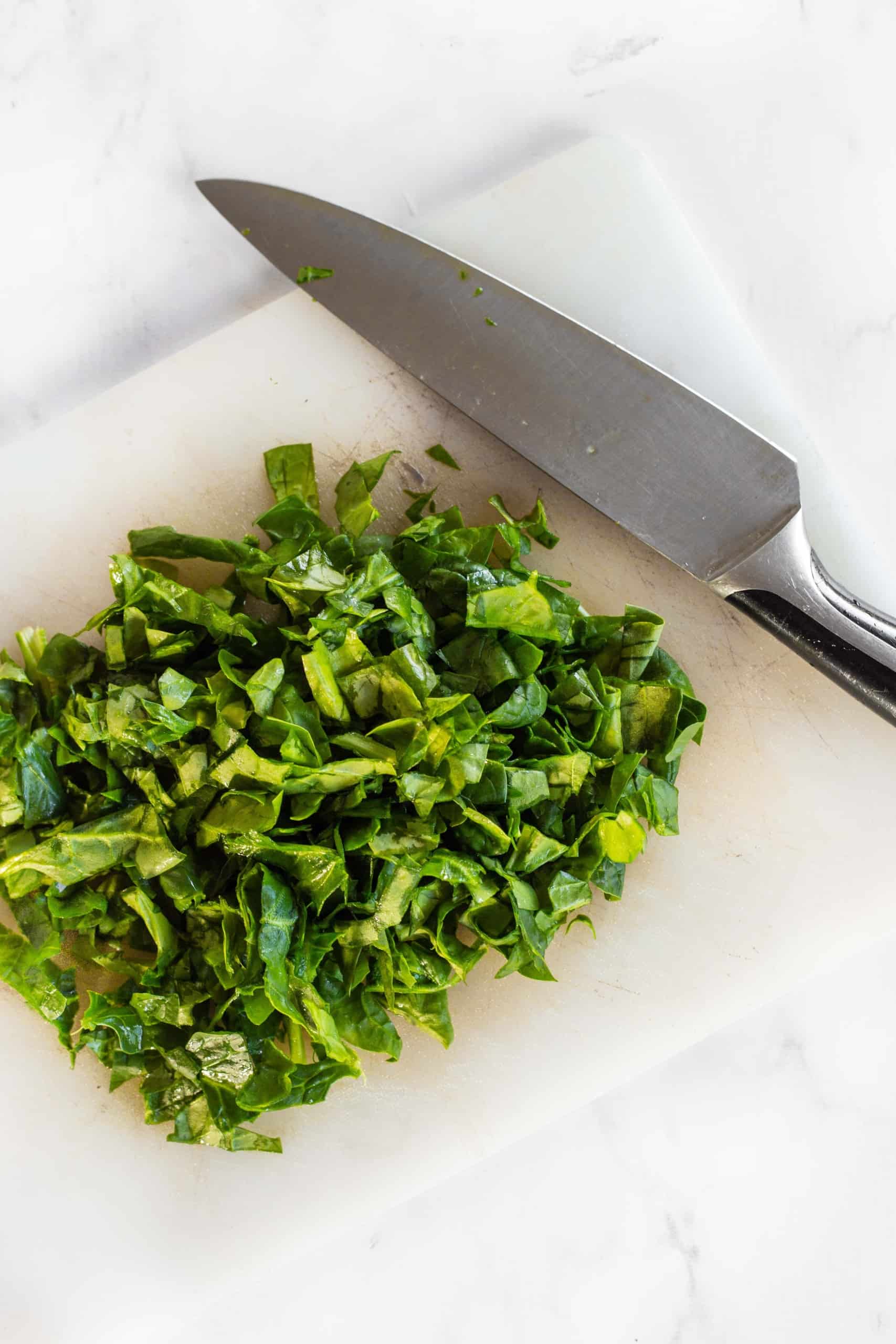 Chopped spinach leaves and large knife on chopping board.