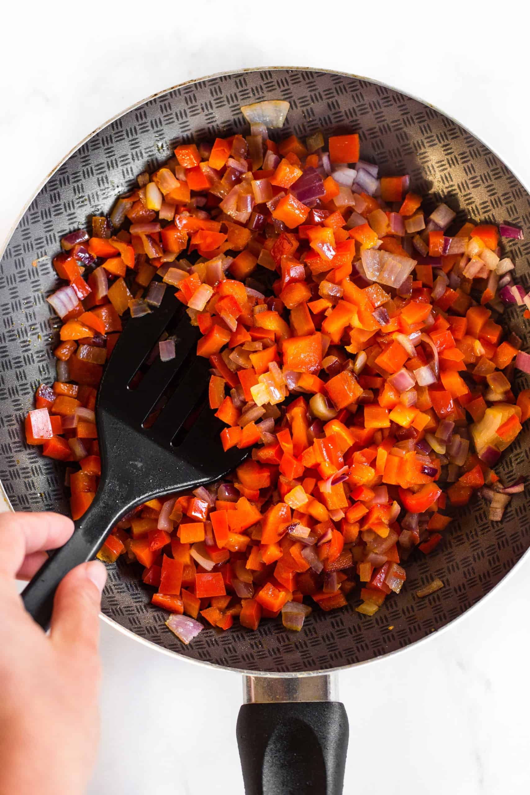 Sautéing diced onions and bell peppers in skillet.