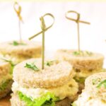 Egg salad tea sandwiches on wooden board.