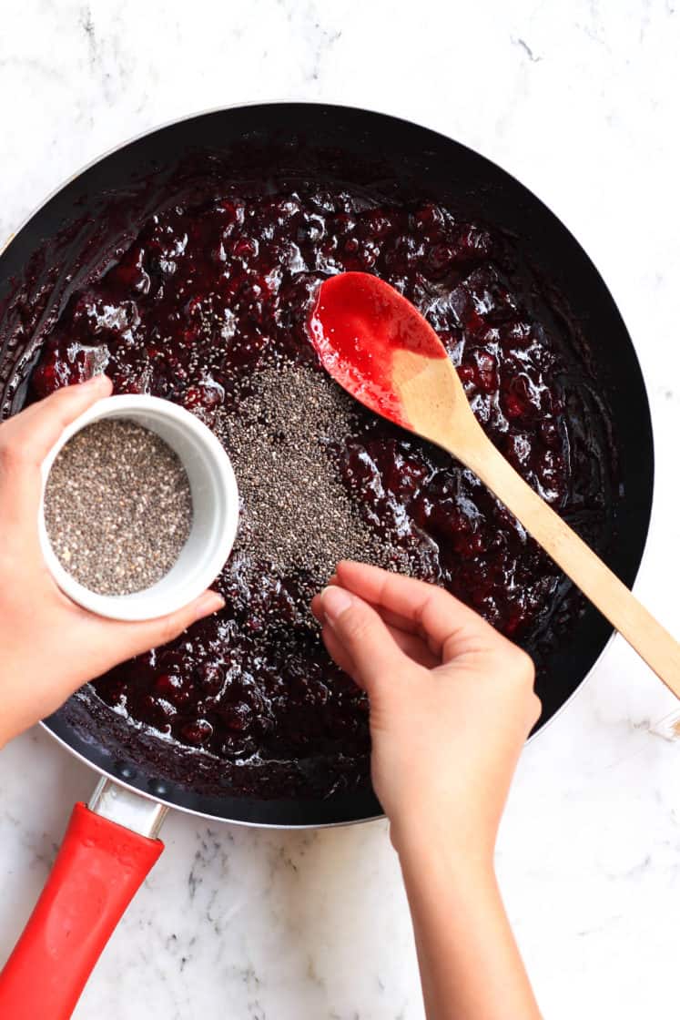 Sprinkling whole chia seeds over cooked fruit mixture in a skillet.