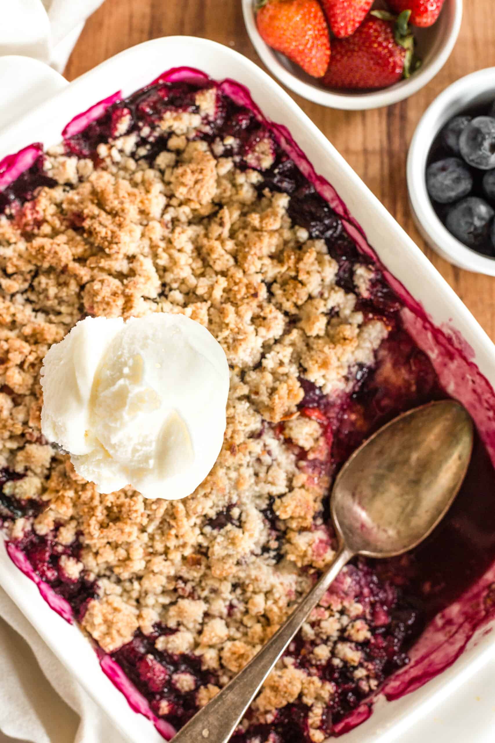 A scoop of vanilla ice cream on top of a dish with half-eaten mixed berry crumble.