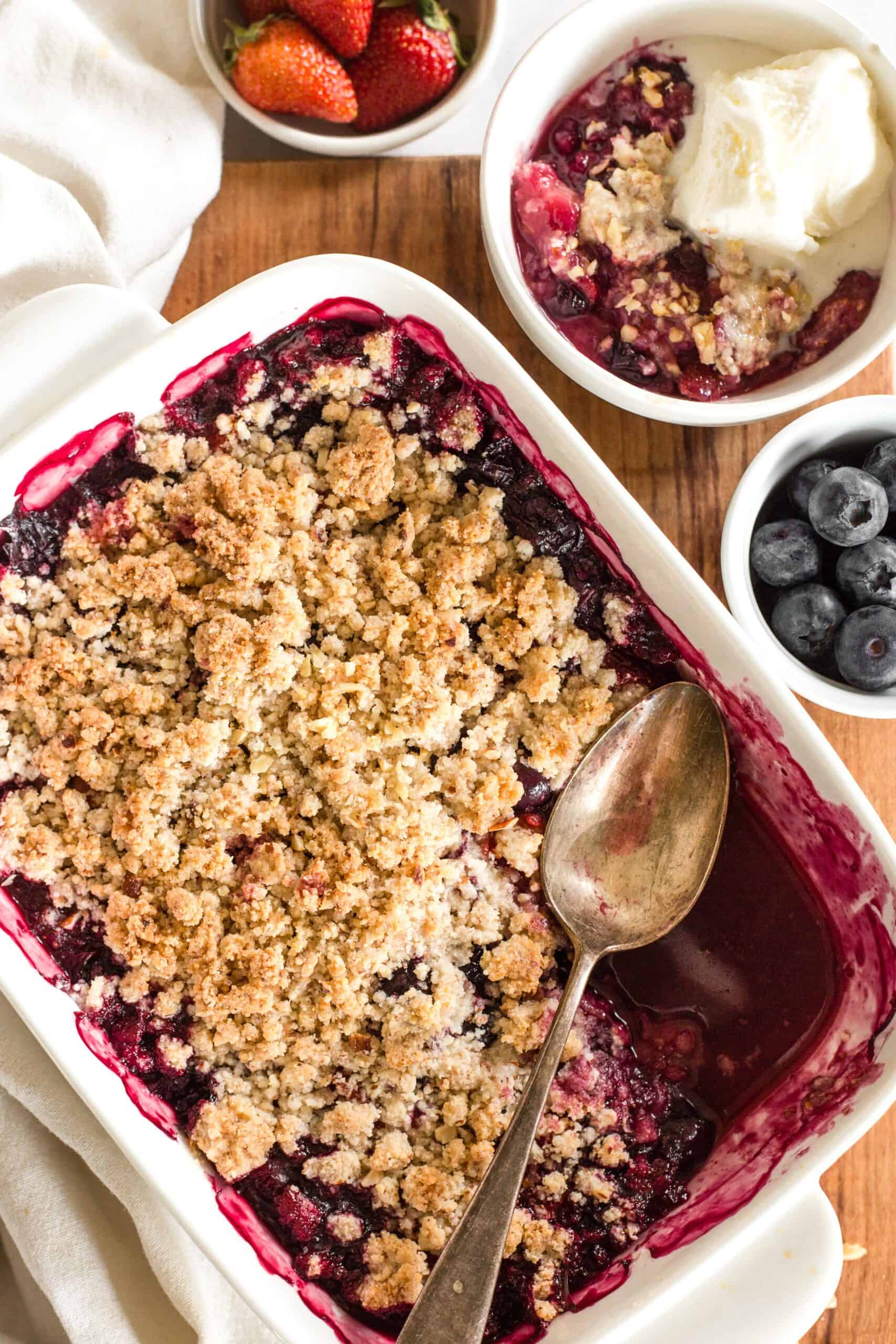Half eaten gluten free berry crumble on wooden board with spoon.