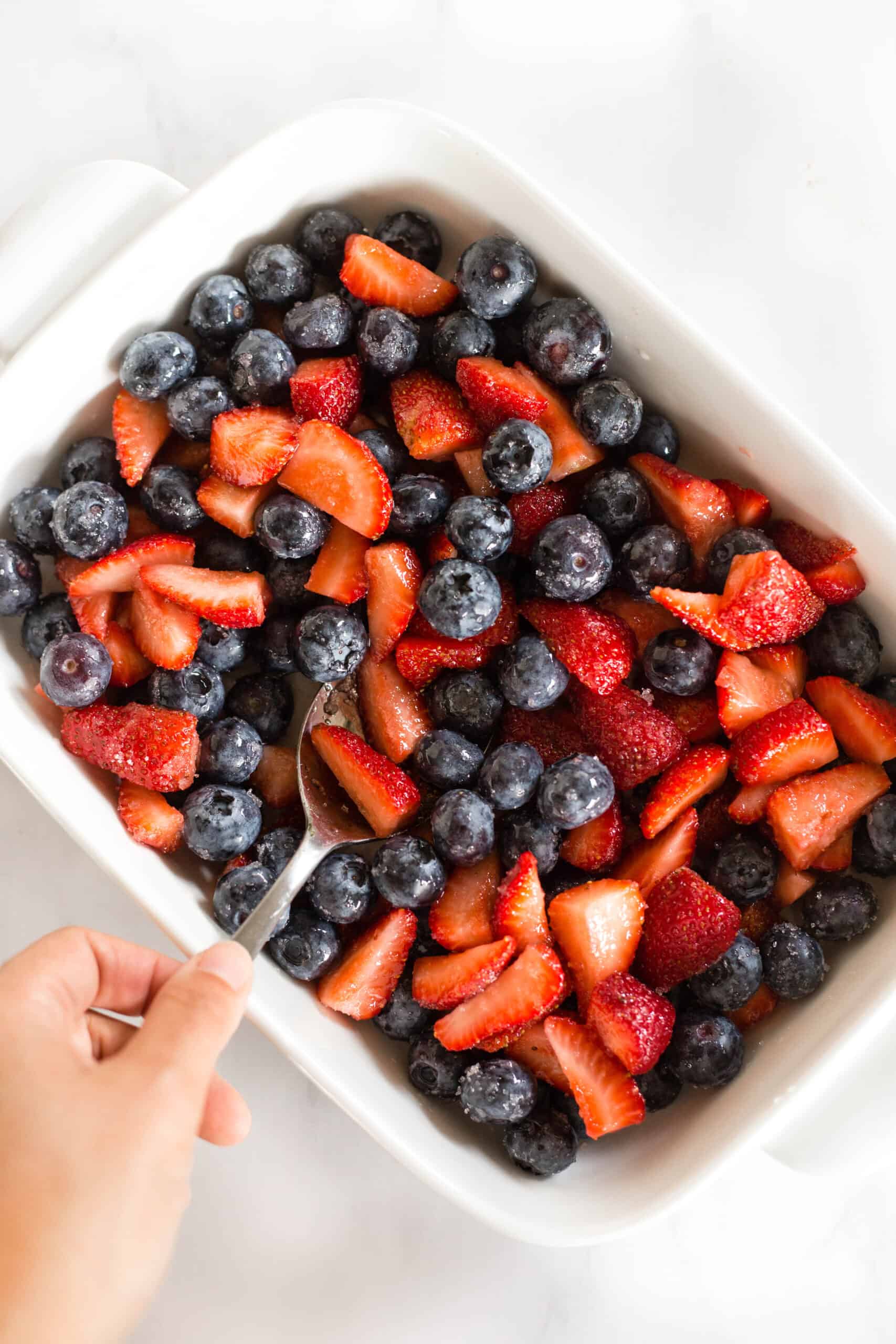 Mixing berries in a large rectangle baking dish.