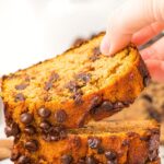 Hand reaching for a slice of almond flour pumpkin bread from a stack.
