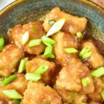 Top down view of a bowl of Mongolian chicken garnished with green onions.