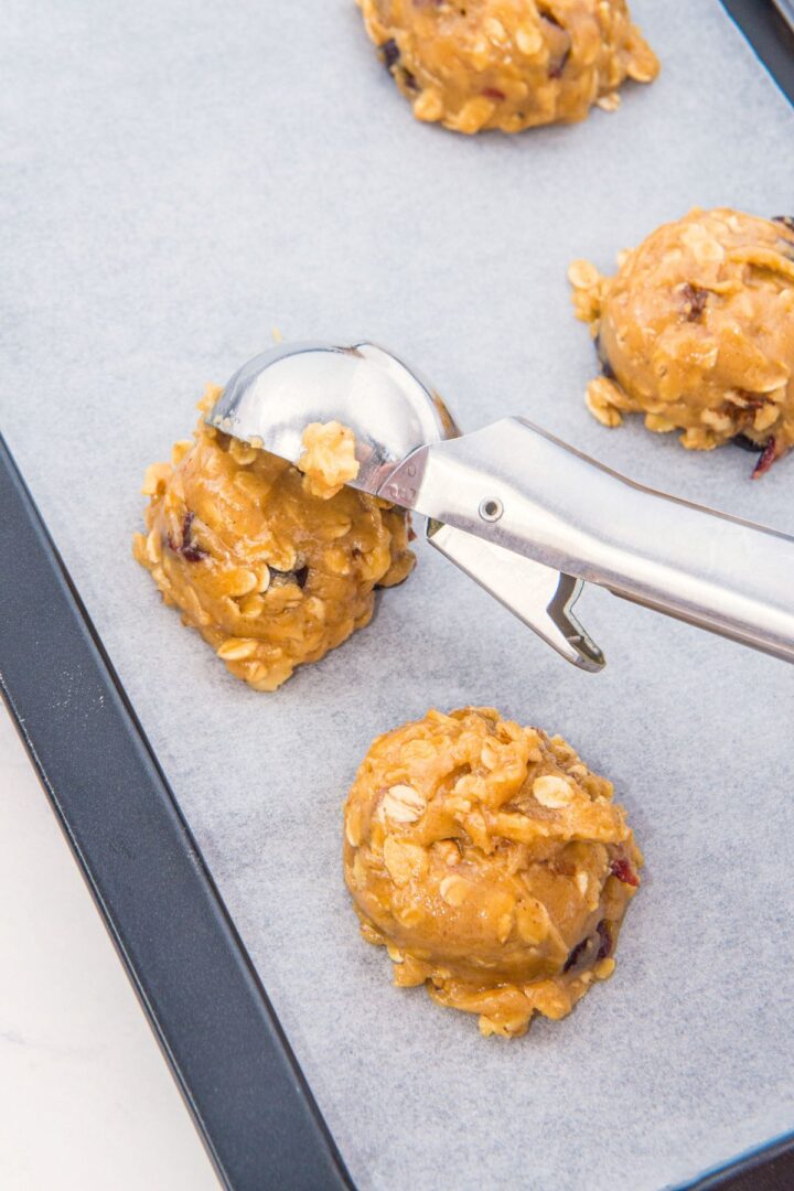 Using cookie scoop to scoop out cookie dough onto parchment-lined baking sheet.