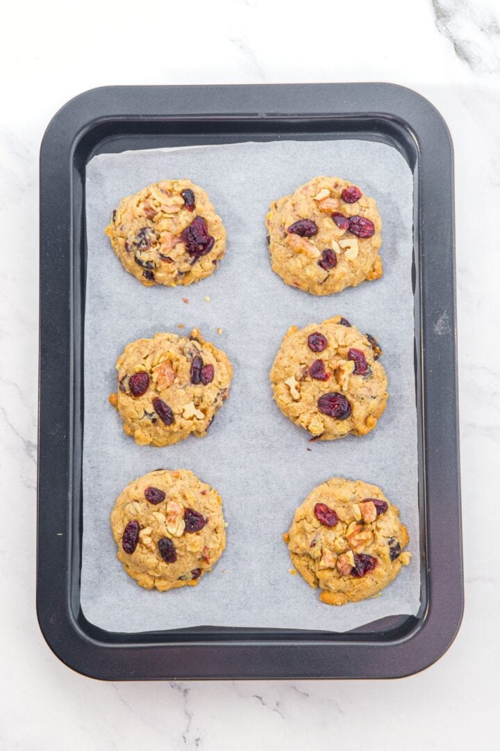 Freshly baked cranberry oatmeal cookies on parchment-lined cookie sheet.